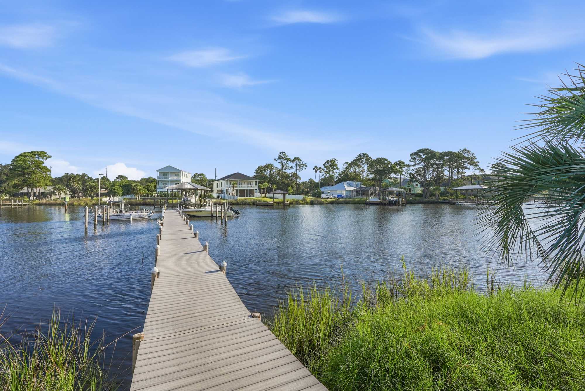 St Thomas SQ 1209C – Dock leading to calm water with nearby houses and greenery under a blue sky.