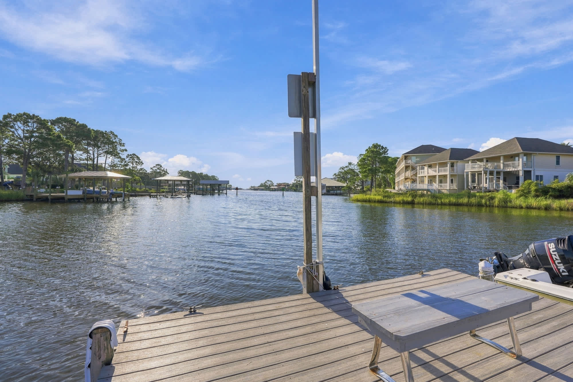St Thomas SQ 1209C – View from dock over calm water, with nearby houses and greenery under a clear blue sky.