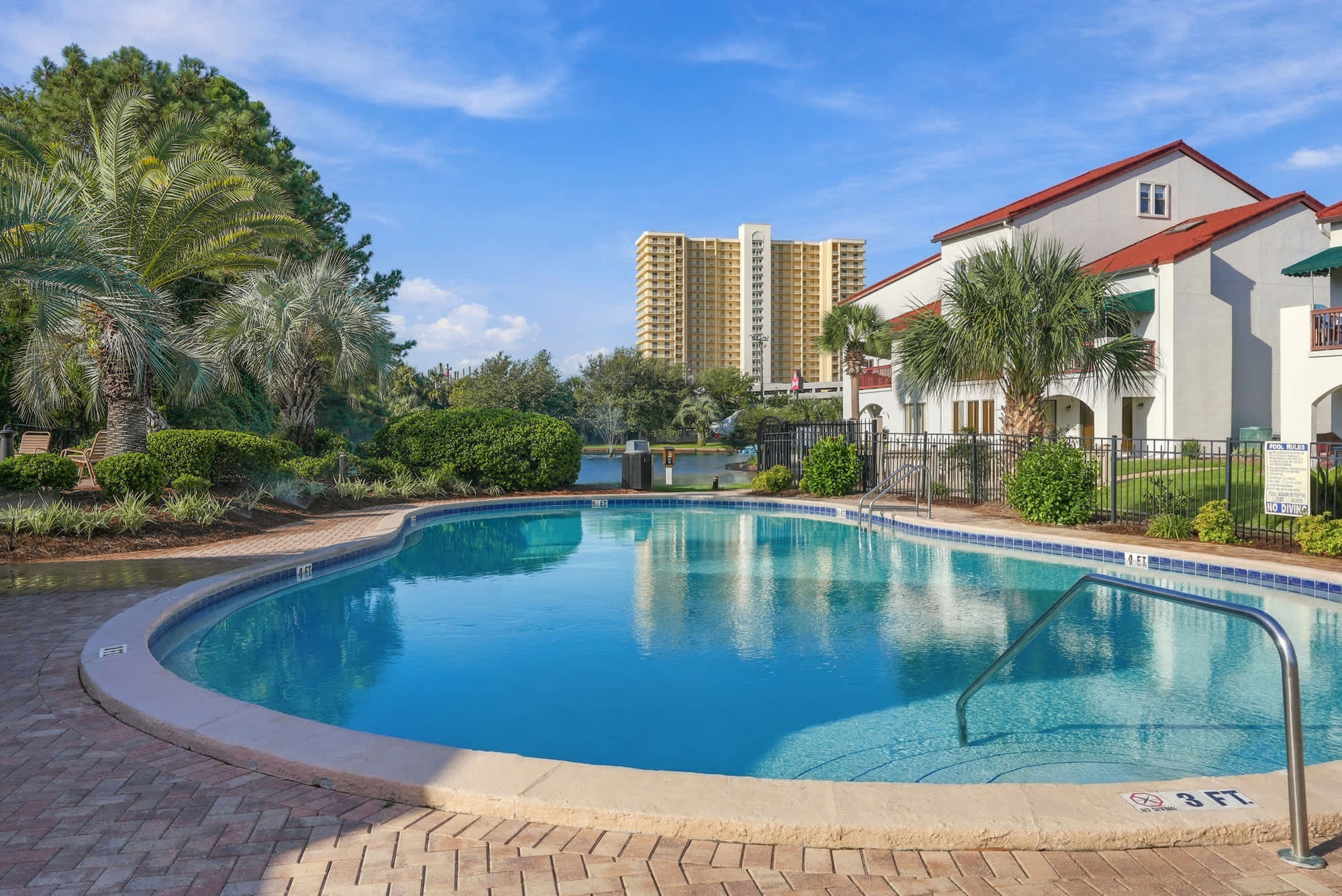 St Thomas SQ 1209C – Pool area surrounded by palm trees and landscaped greenery, with a residential building in the background.
