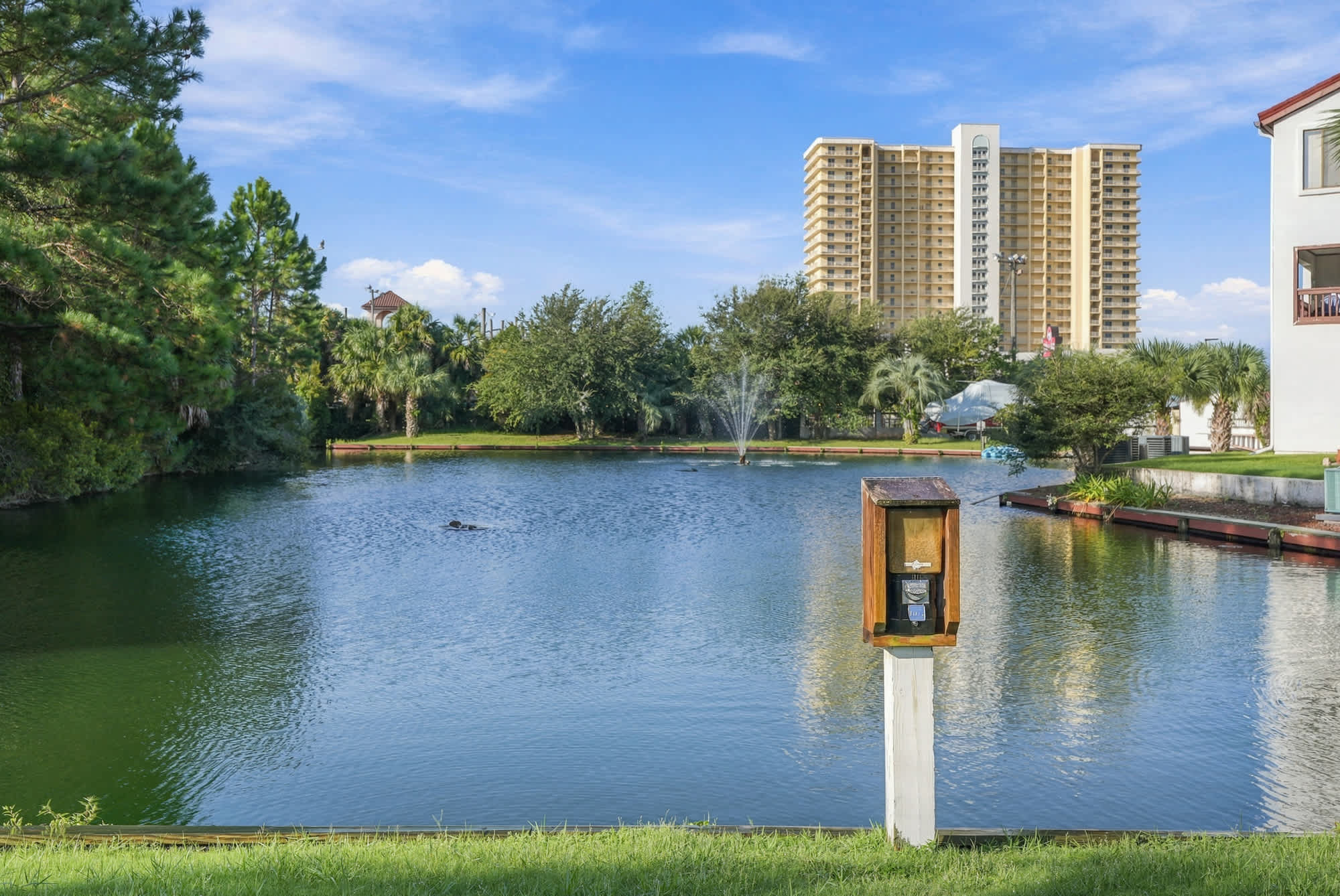 St Thomas SQ 1209C – Lakeside view with fountain, greenery, and nearby tall building.