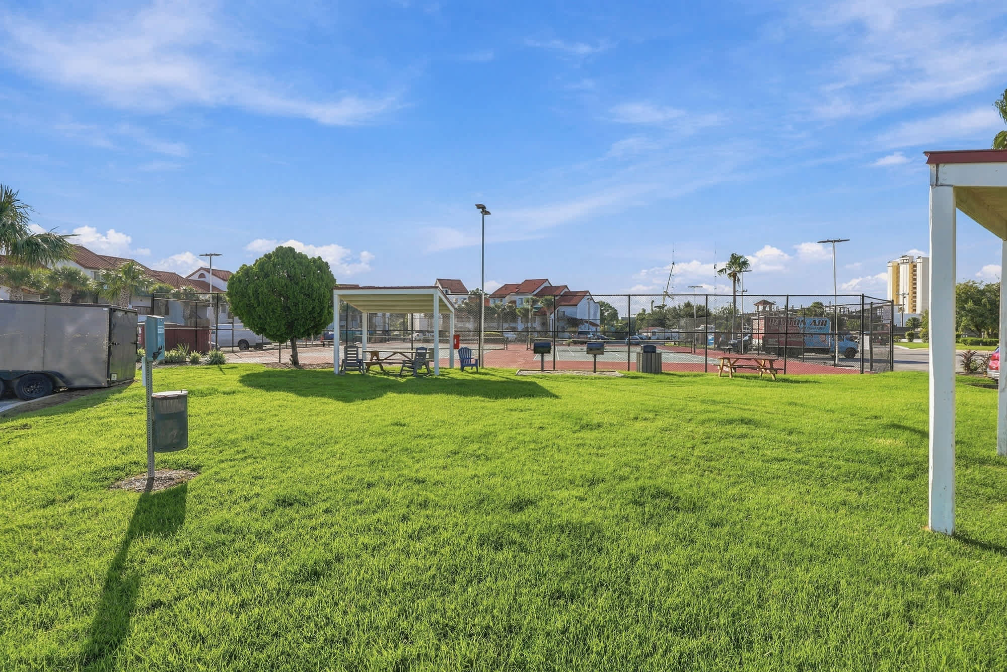 St Thomas SQ 1209C – Green grassy area with picnic table, trees, and view of tennis courts and buildings in the background.
