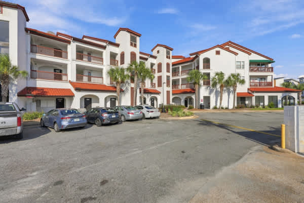 St Thomas SQ 1302B – Three-story vacation rental building with palm trees and parking area, blue sky above.