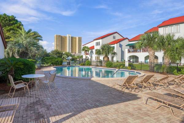 St Thomas SQ 1302B – Pool area with lounge chairs, surrounded by palm trees and buildings under a blue sky.
