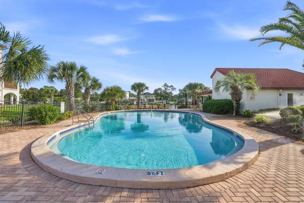 St Thomas SQ 1302B – Curved swimming pool surrounded by palm trees and brick patio, with blue sky in the background.
