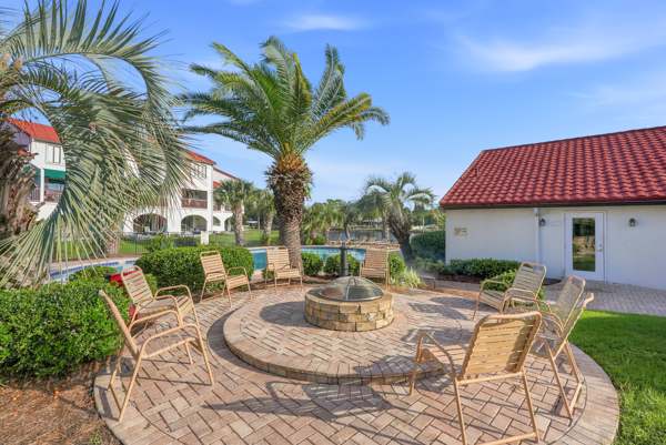 St Thomas SQ 1302B – Patio area with a fire pit surrounded by chairs, palm trees, and a nearby building with a red roof.