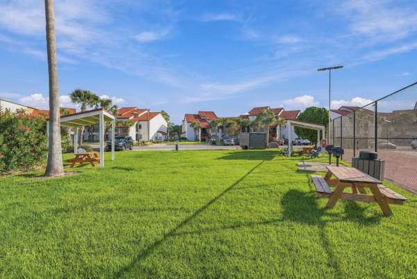 St Thomas SQ 1302B – Green lawn with picnic tables, surrounded by buildings and a tennis court in the background.