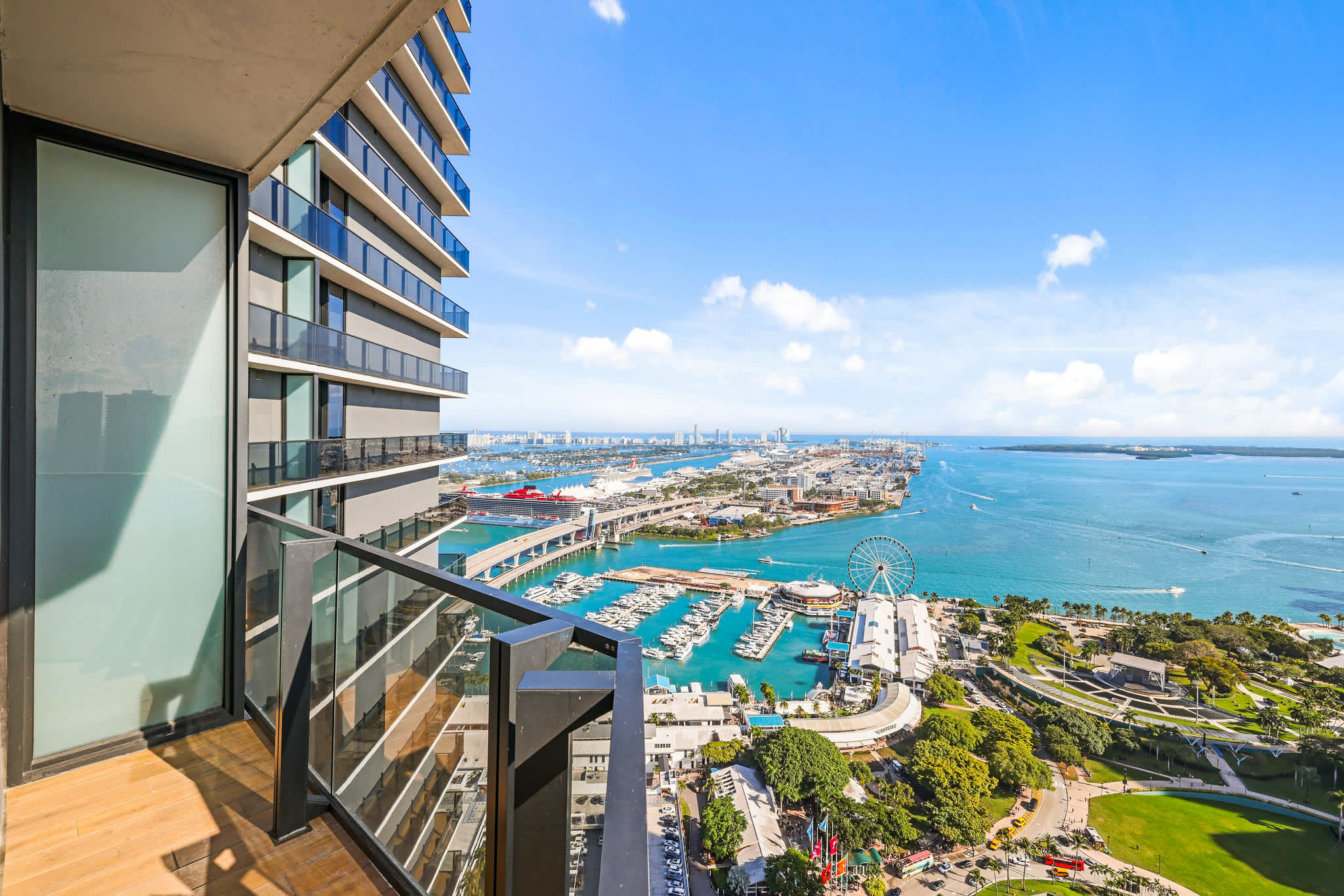 Private balcony with sweeping views of the turquoise waterfront, marina, cruise ships, Ferris wheel, and city skyline.
