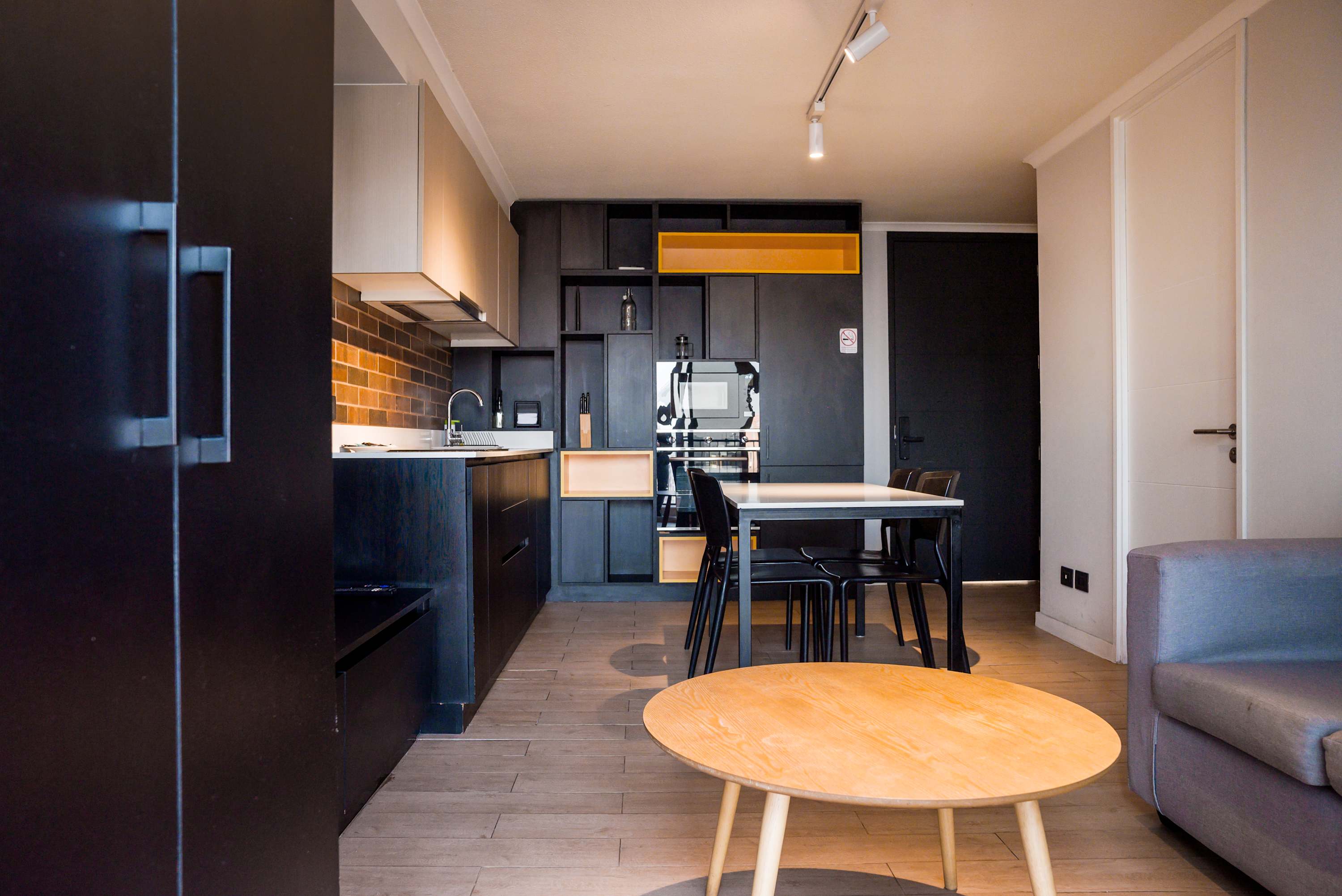 Open-plan kitchen and dining area with matte black cabinetry, a mustard-yellow display shelf, and a four-seat table beside the living room.