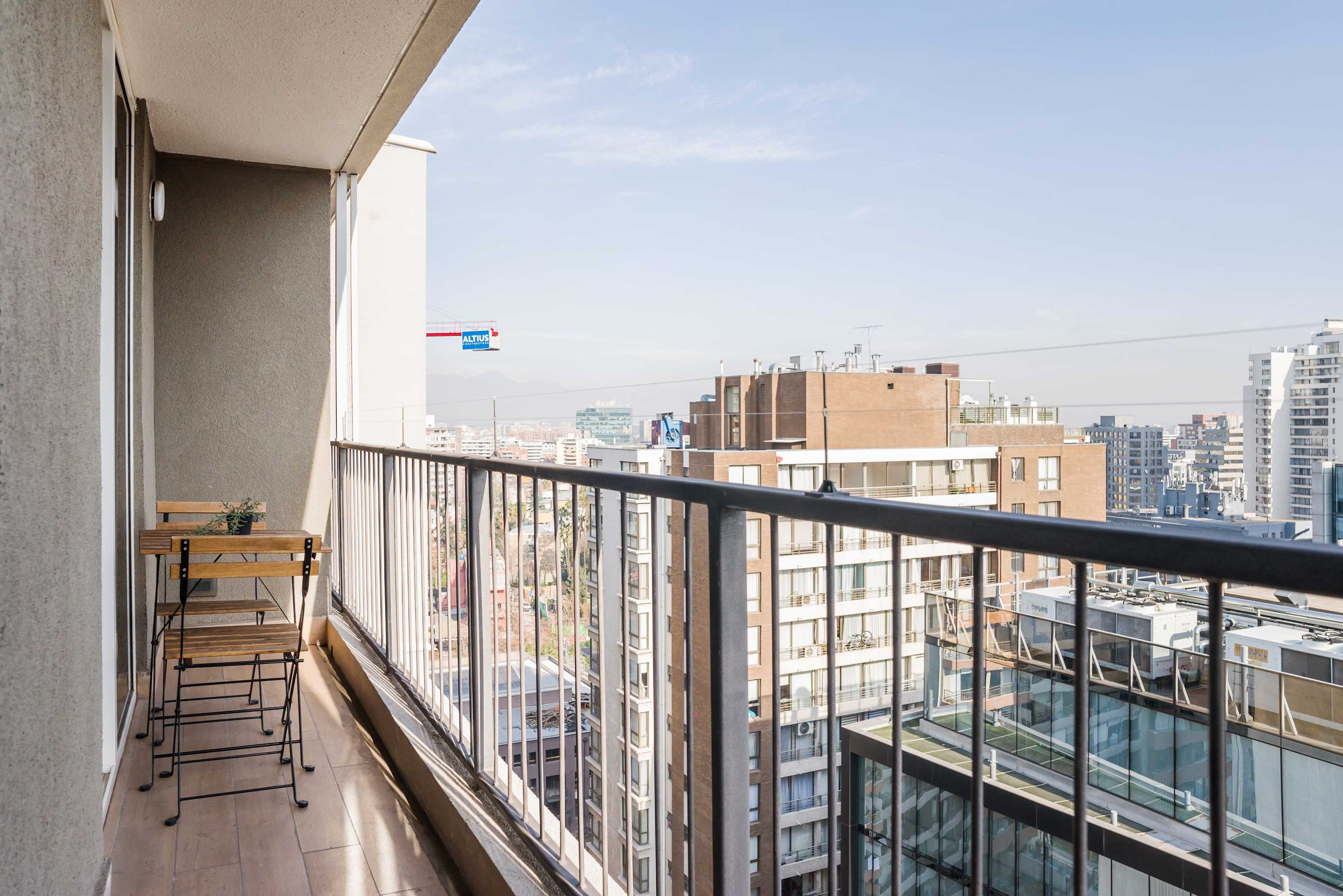 Private balcony with a two-person wooden bistro set and expansive views over the city skyline.