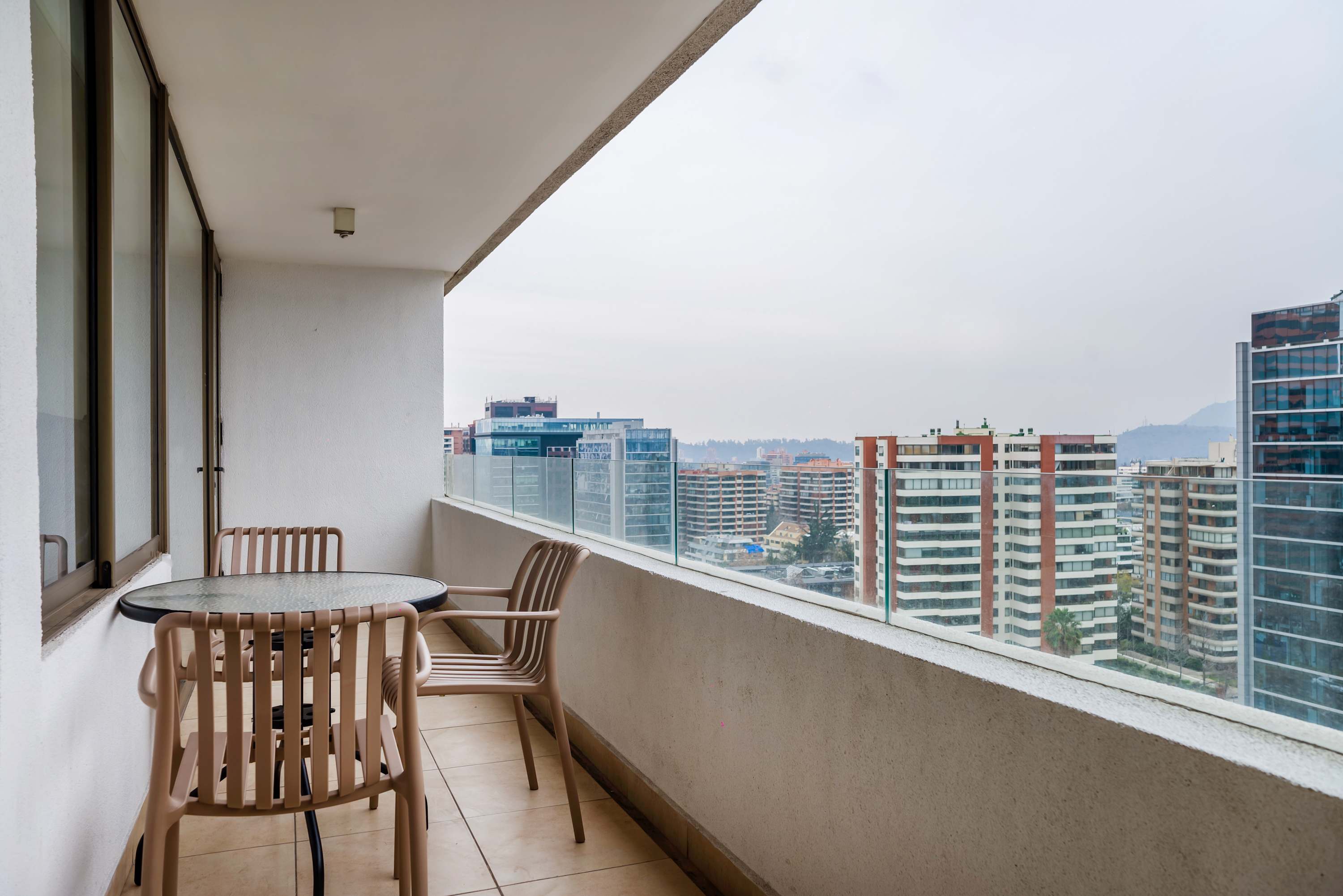 Private balcony with a round outdoor dining table, five chairs, and expansive views across the city skyline to the distant hills.