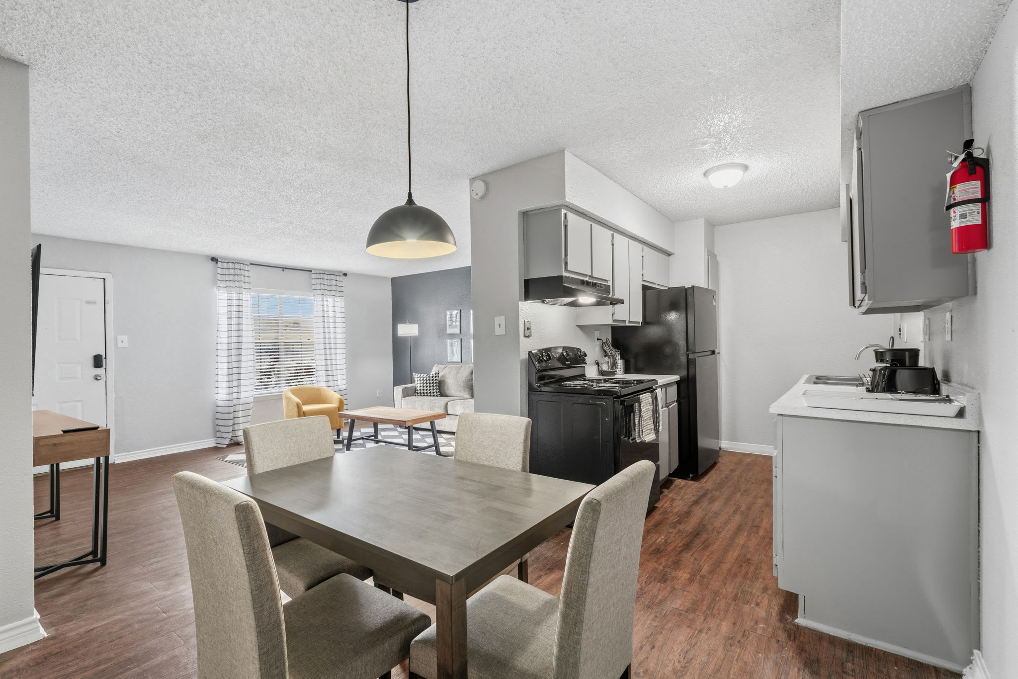 Open-plan dining and living area with seating for six, a full kitchen, and abundant daylight through the striped-curtain window.