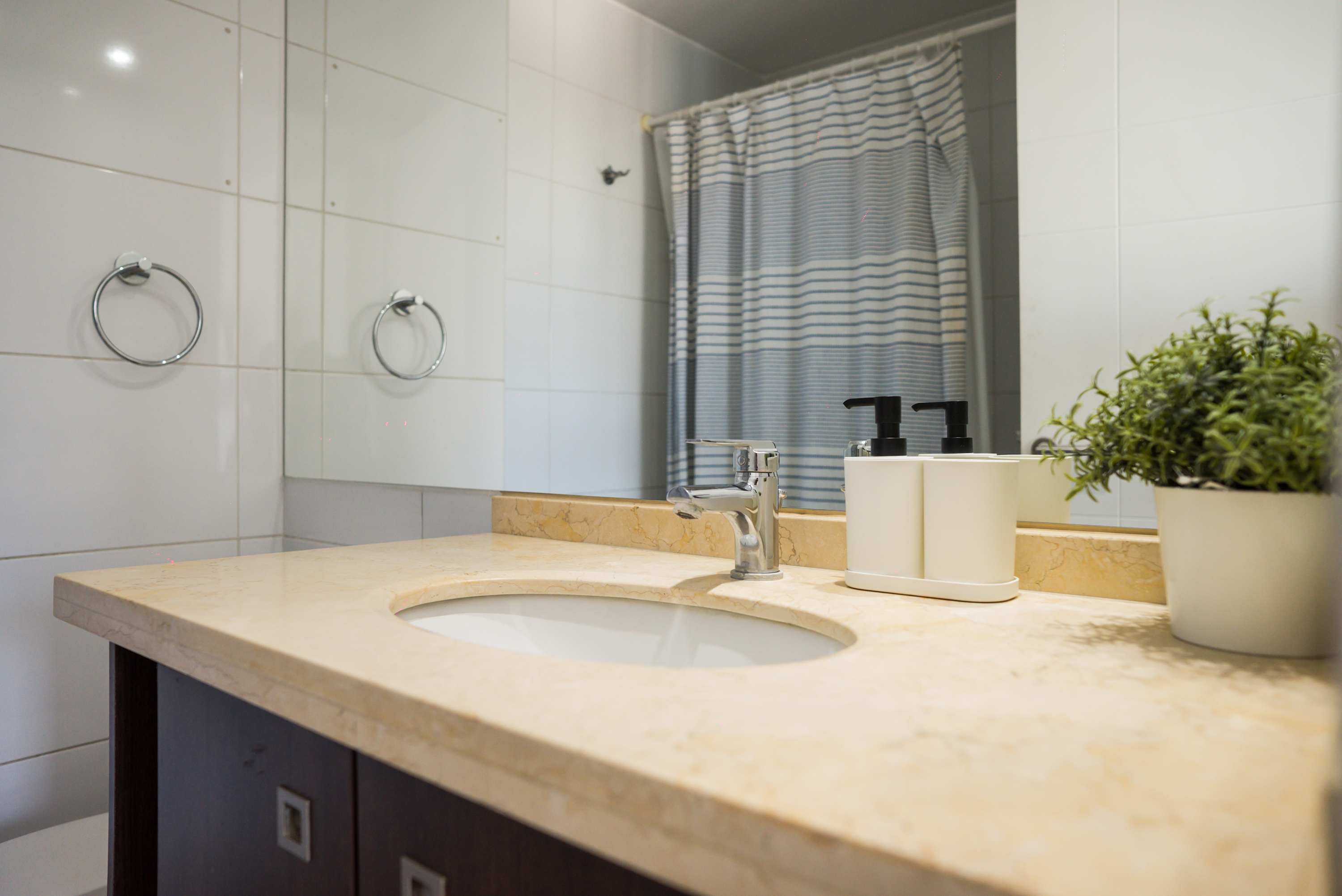 Private bathroom with a marble-look vanity, oval sink, chrome fixtures, and a blue-and-white striped shower curtain.