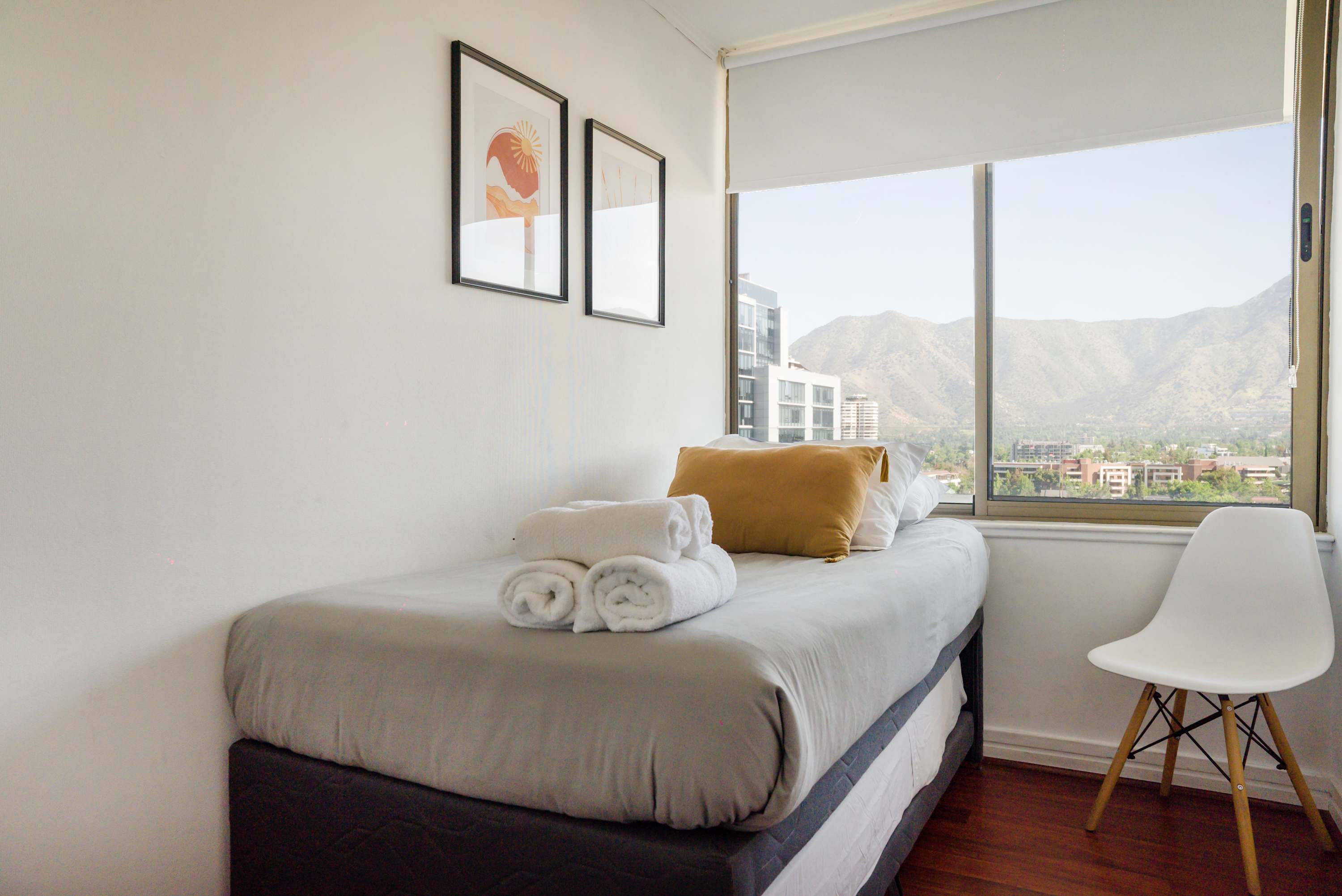 Bright bedroom with crisp white linens, rolled towels, and a wide window overlooking the Andes mountains.