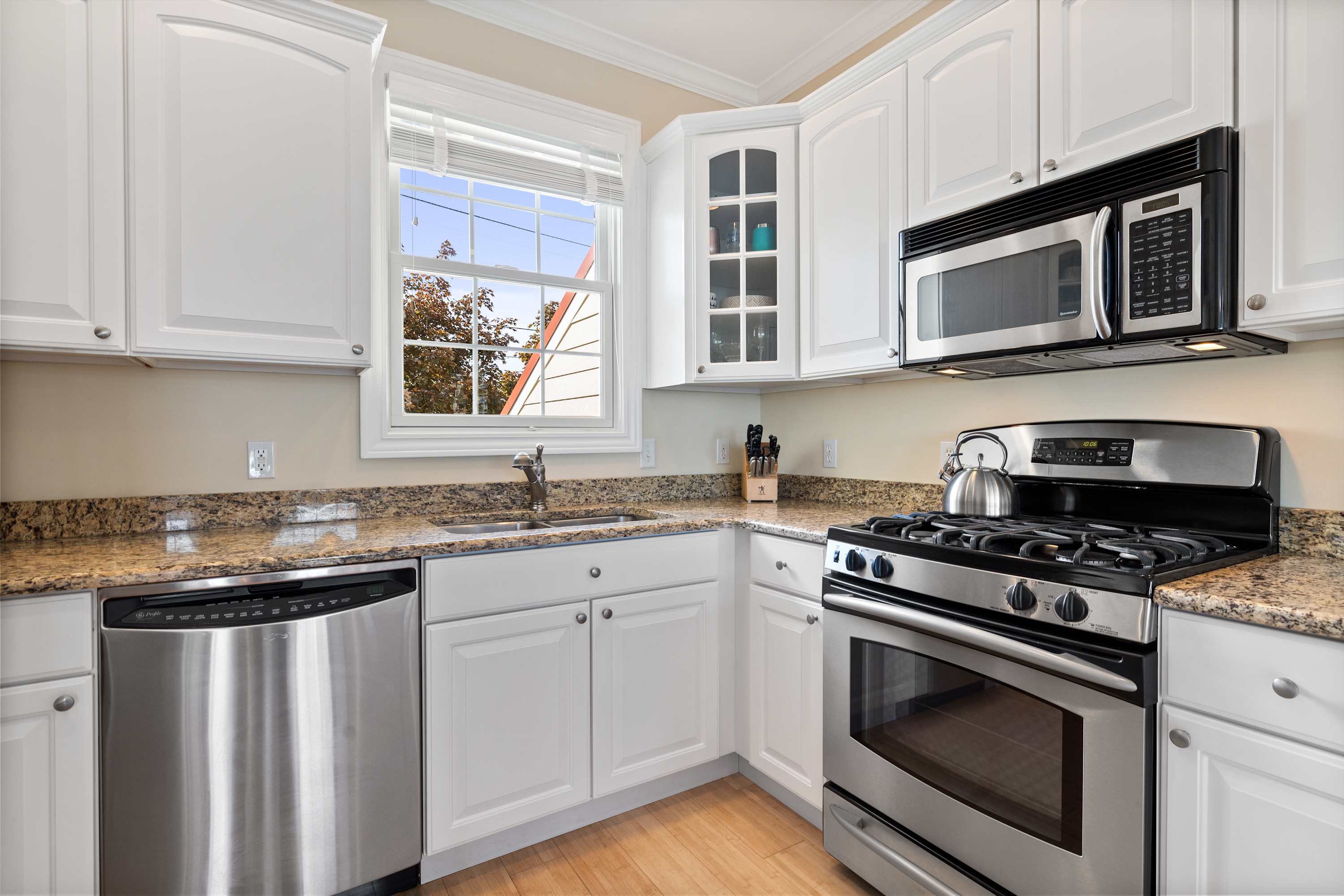 Granite counters and stainless appliances in a bright white kitchen.