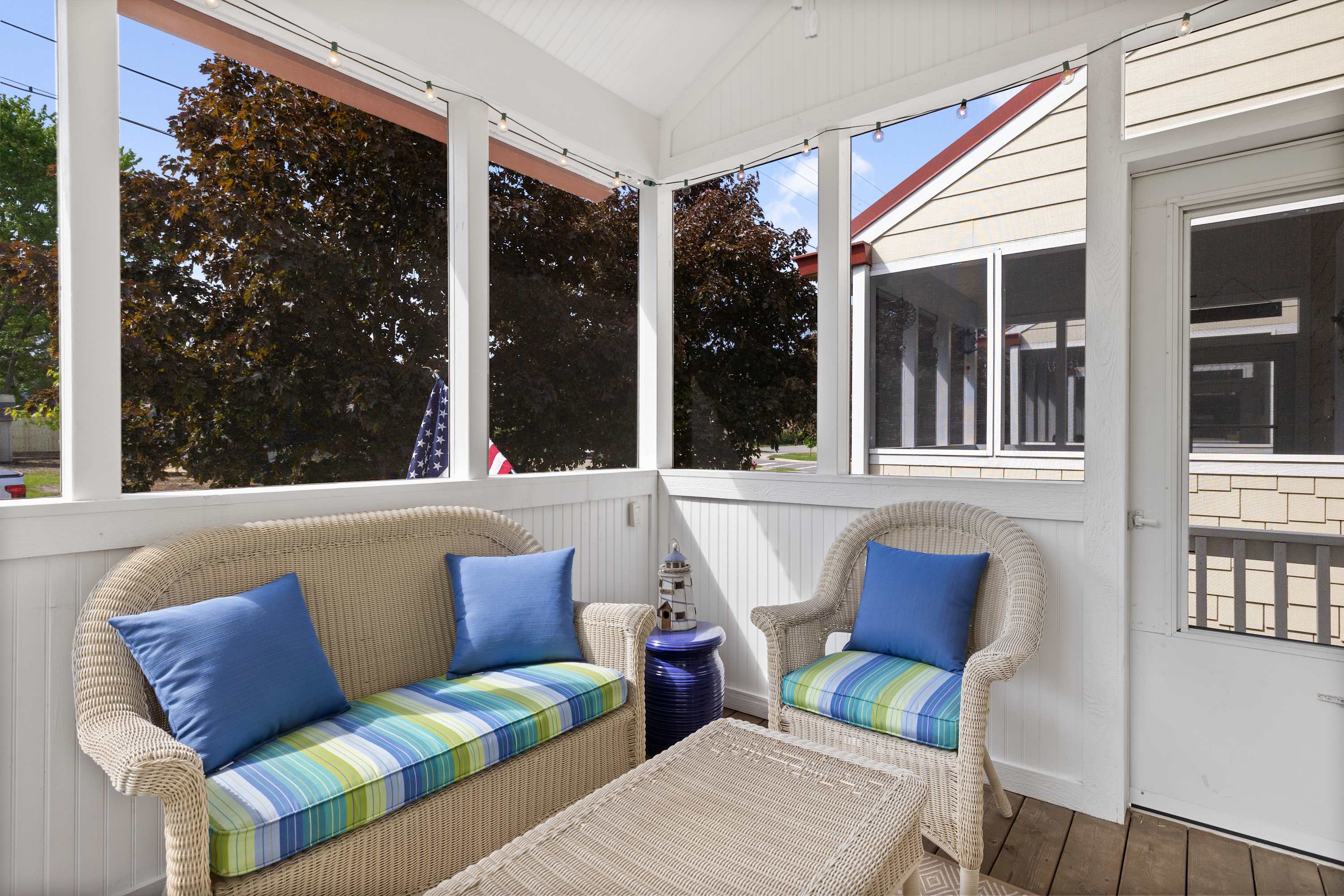 Screened front porch with cushioned wicker seating under shade trees.