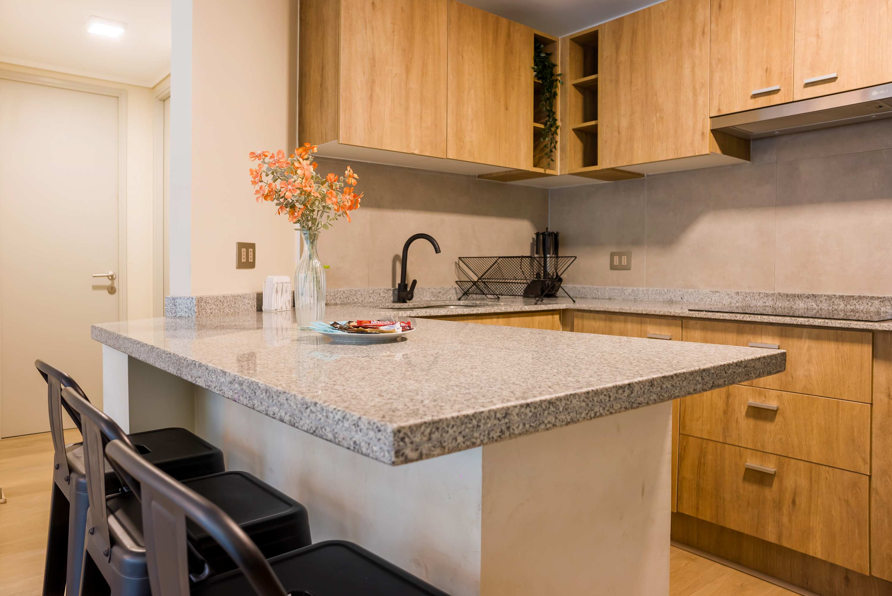 Private kitchen with warm wood cabinetry, a spacious granite peninsula, black fixtures, and seating for shared meals or morning coffee.