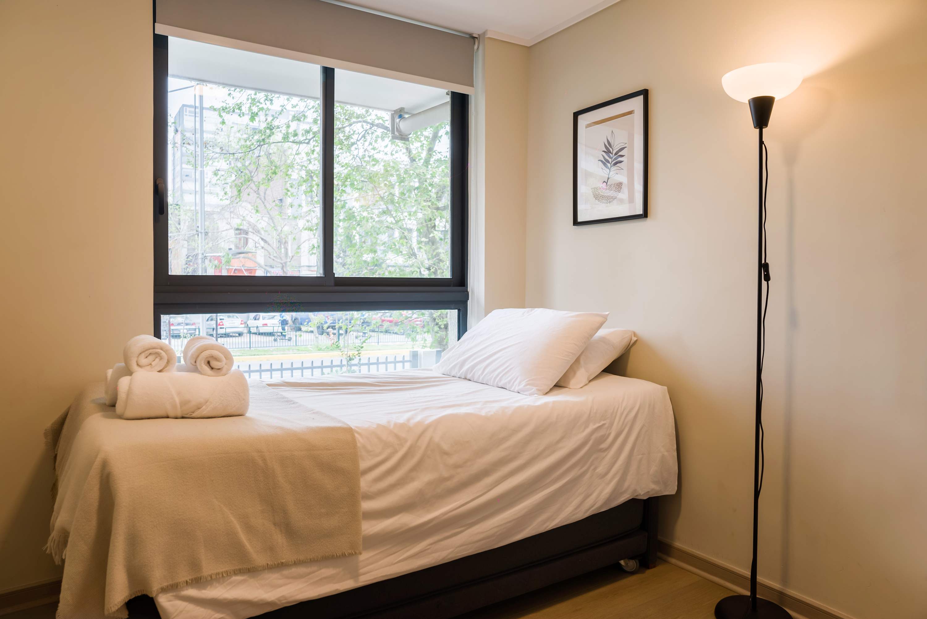 Inviting bedroom with crisp white bedding, rolled towels, and a large window overlooking leafy surroundings.