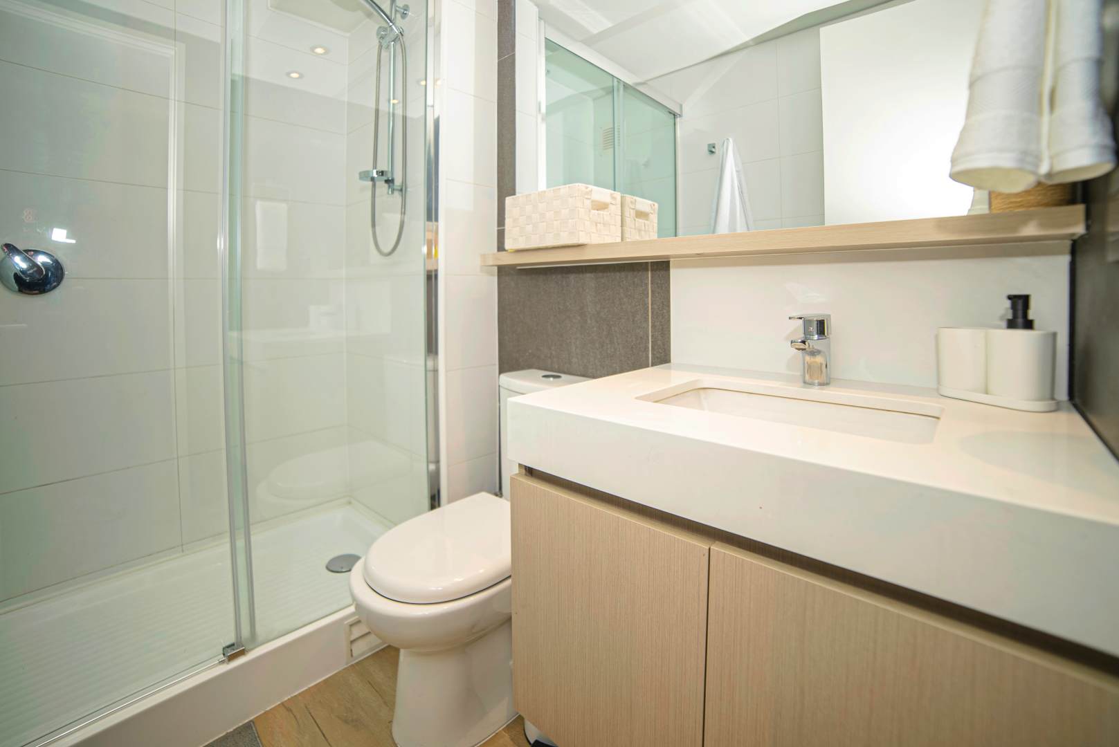 Private bathroom with a glass walk-in shower, integrated white vanity, and warm light-wood cabinetry.
