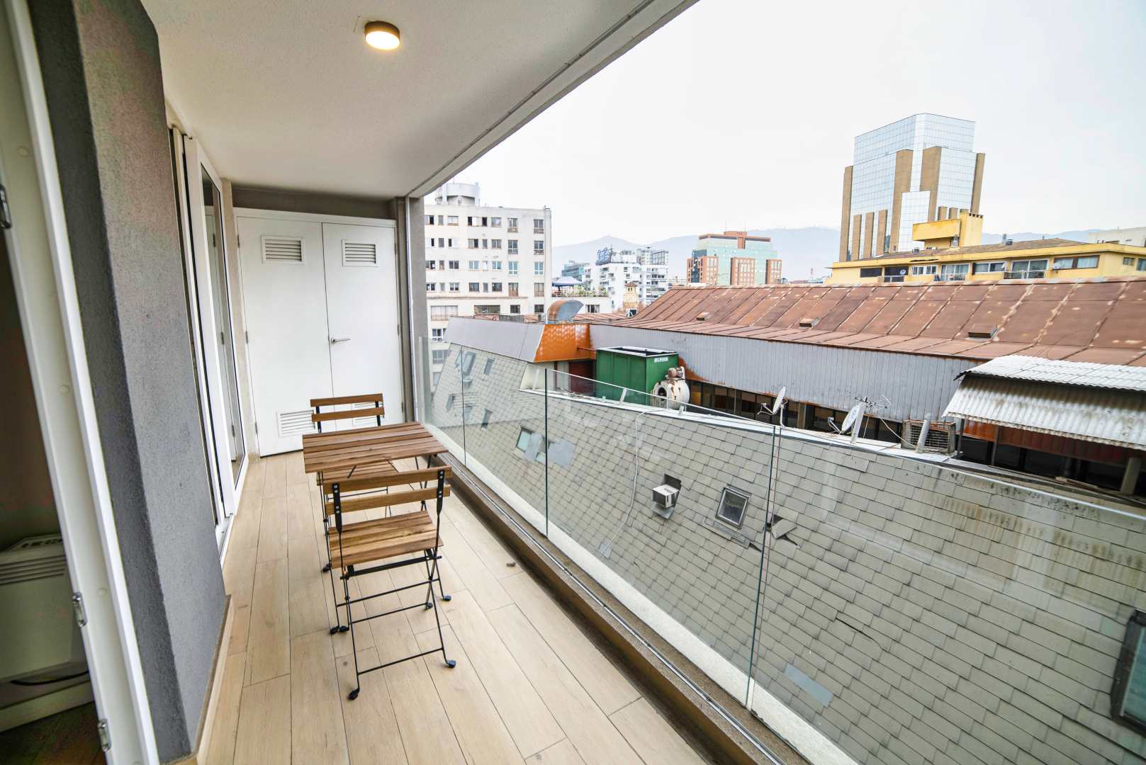 Private balcony with a compact wood dining set and sweeping city views toward the mountains.
