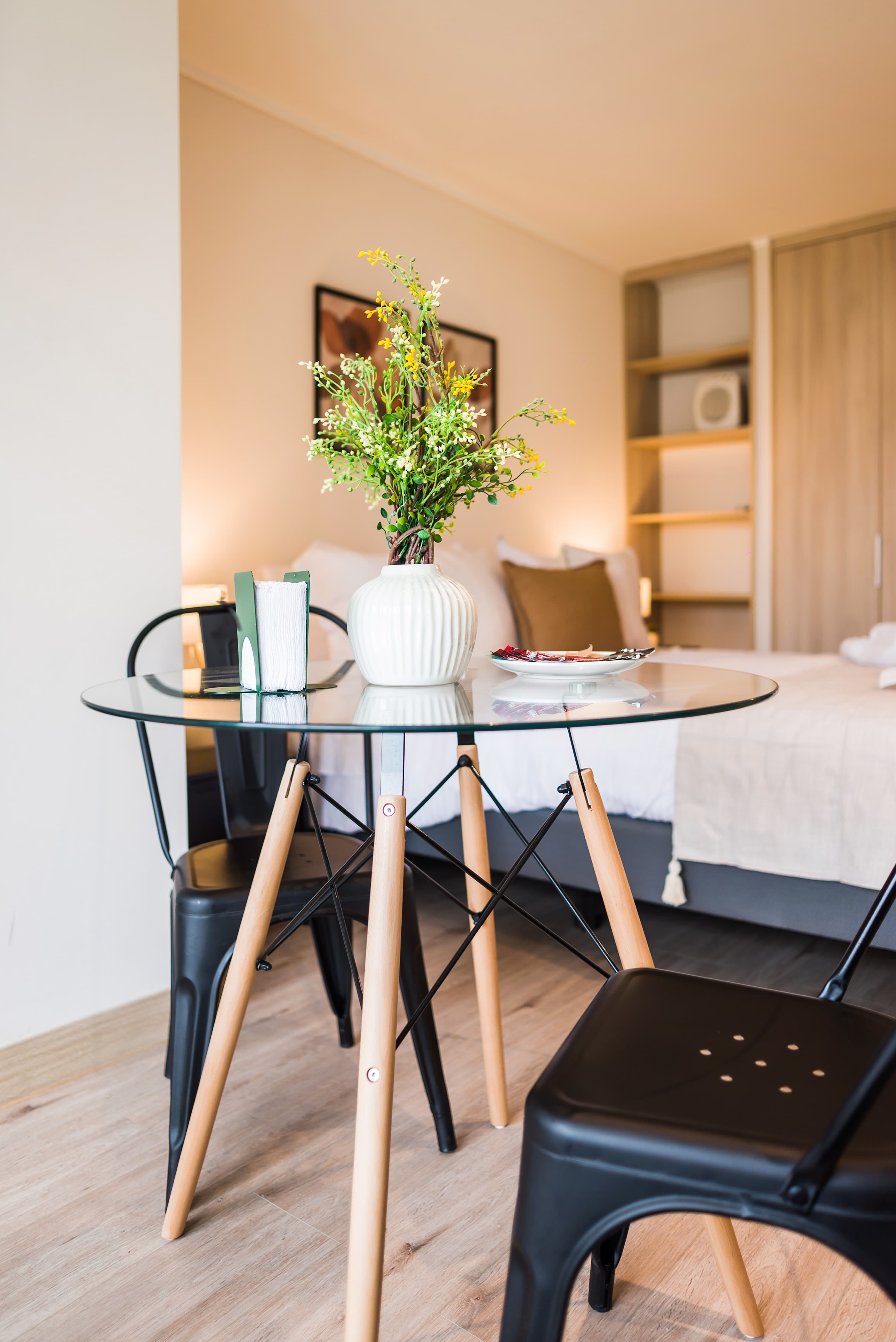 Dining area with a round glass table, sculptural white vase, and coordinated wood-and-black chairs in the studio.