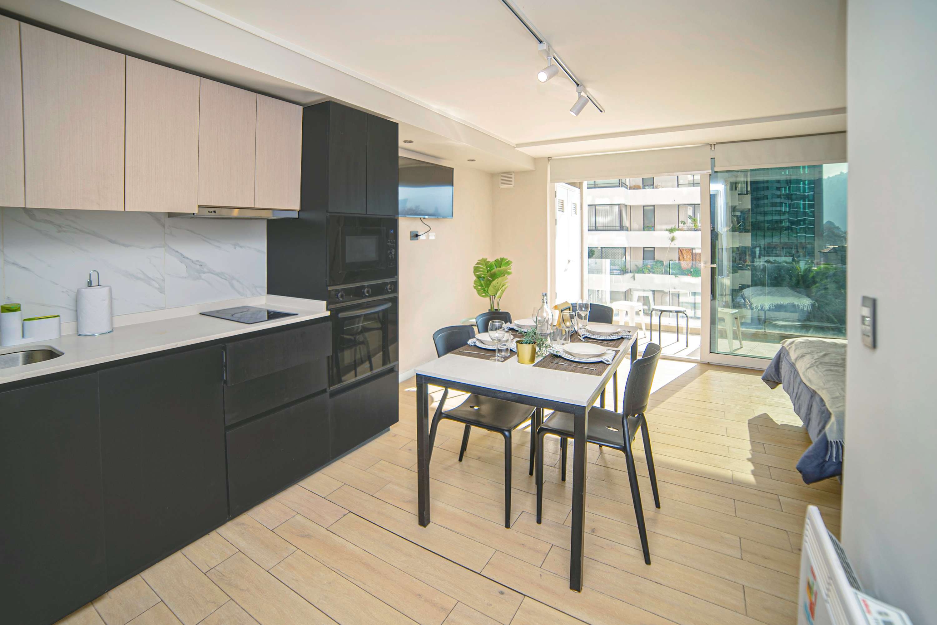 Modern studio kitchen with marble-look backsplash, built-in appliances, and a welcoming dining table set beside bright floor-to-ceiling windows.