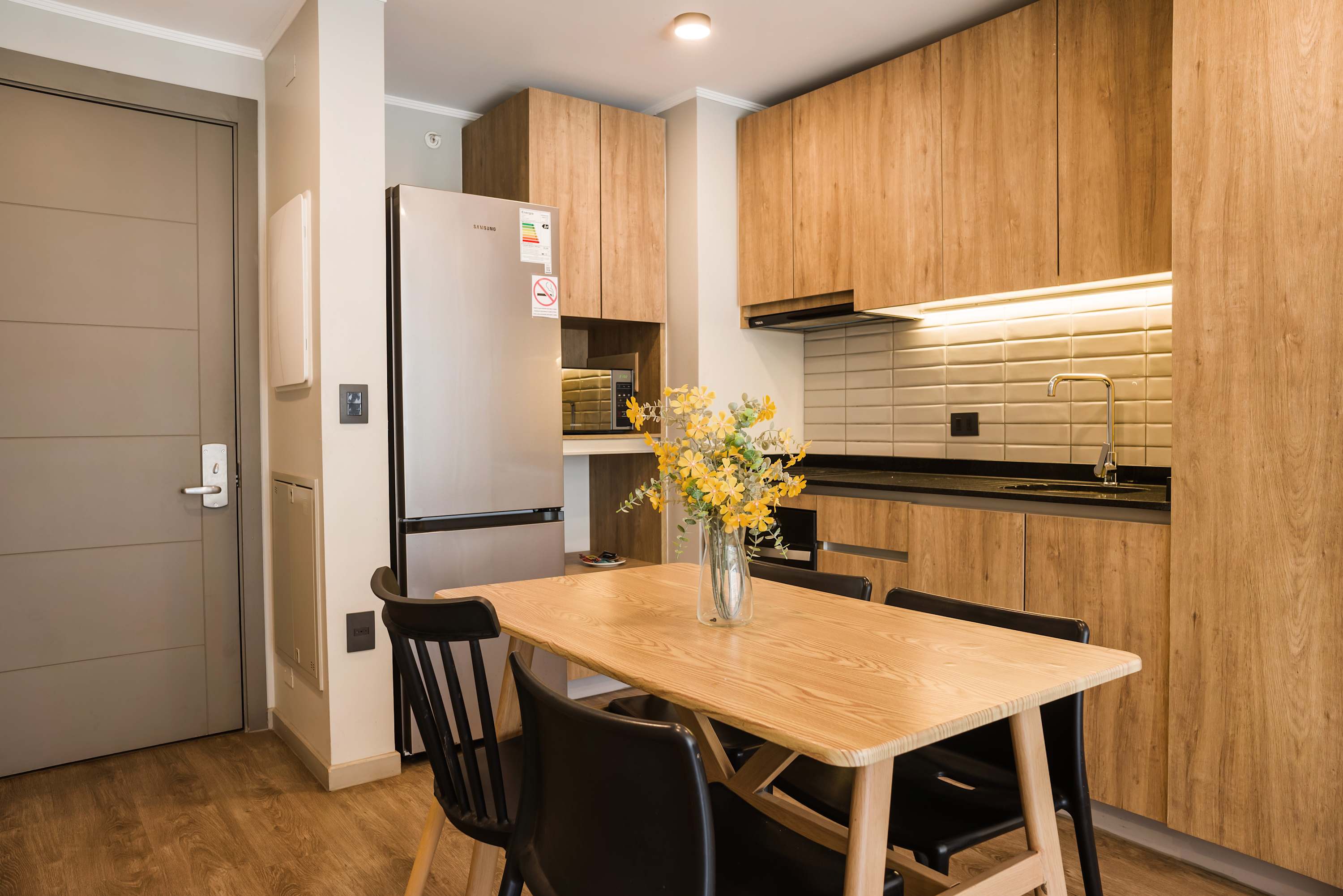 Private kitchen and dining area with warm wood cabinetry, a full-size refrigerator, and seating for five around a light wood table.