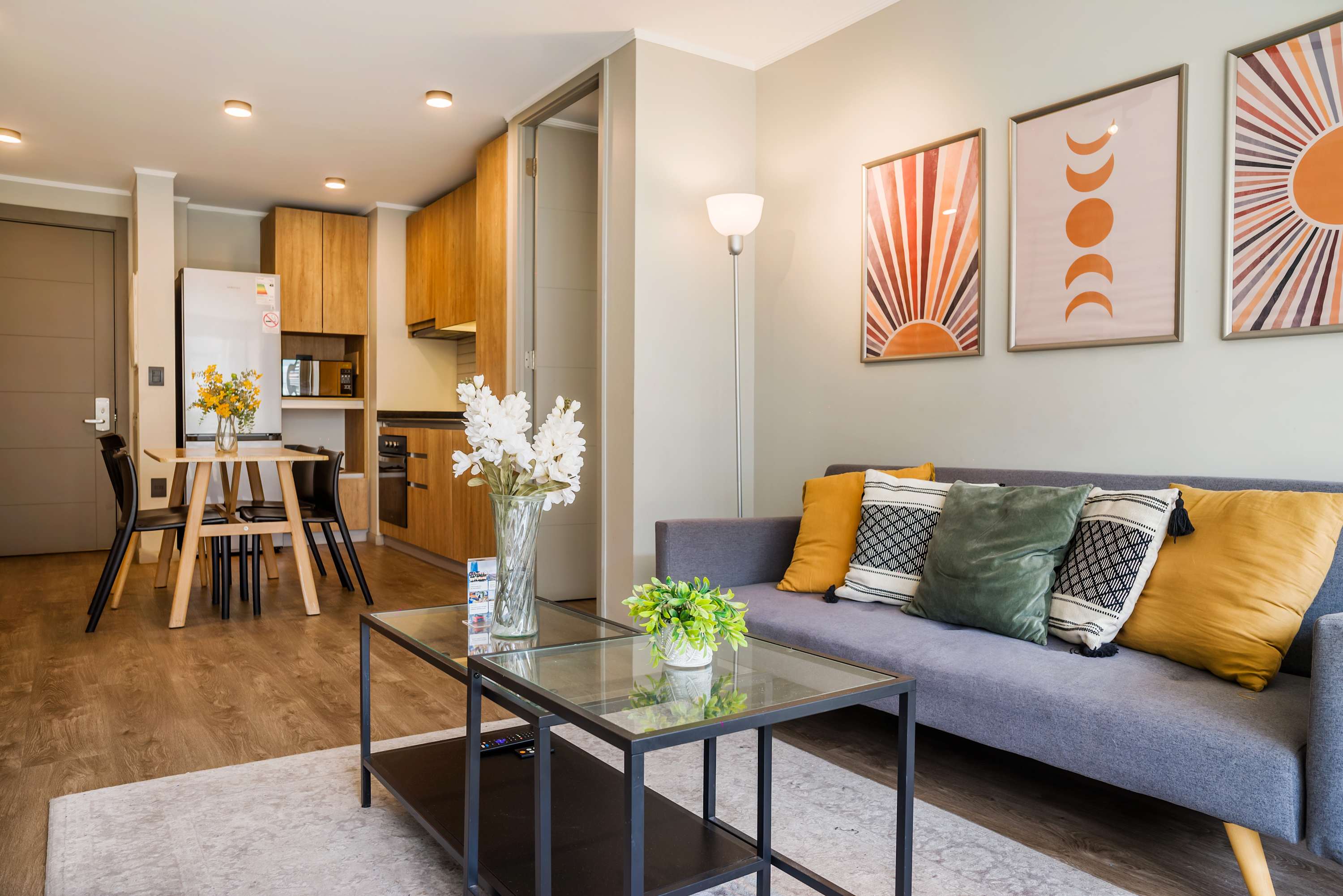 Inviting open-plan living room with a gray sectional, colorful cushions, and a connected dining area beside the warm wood kitchen.