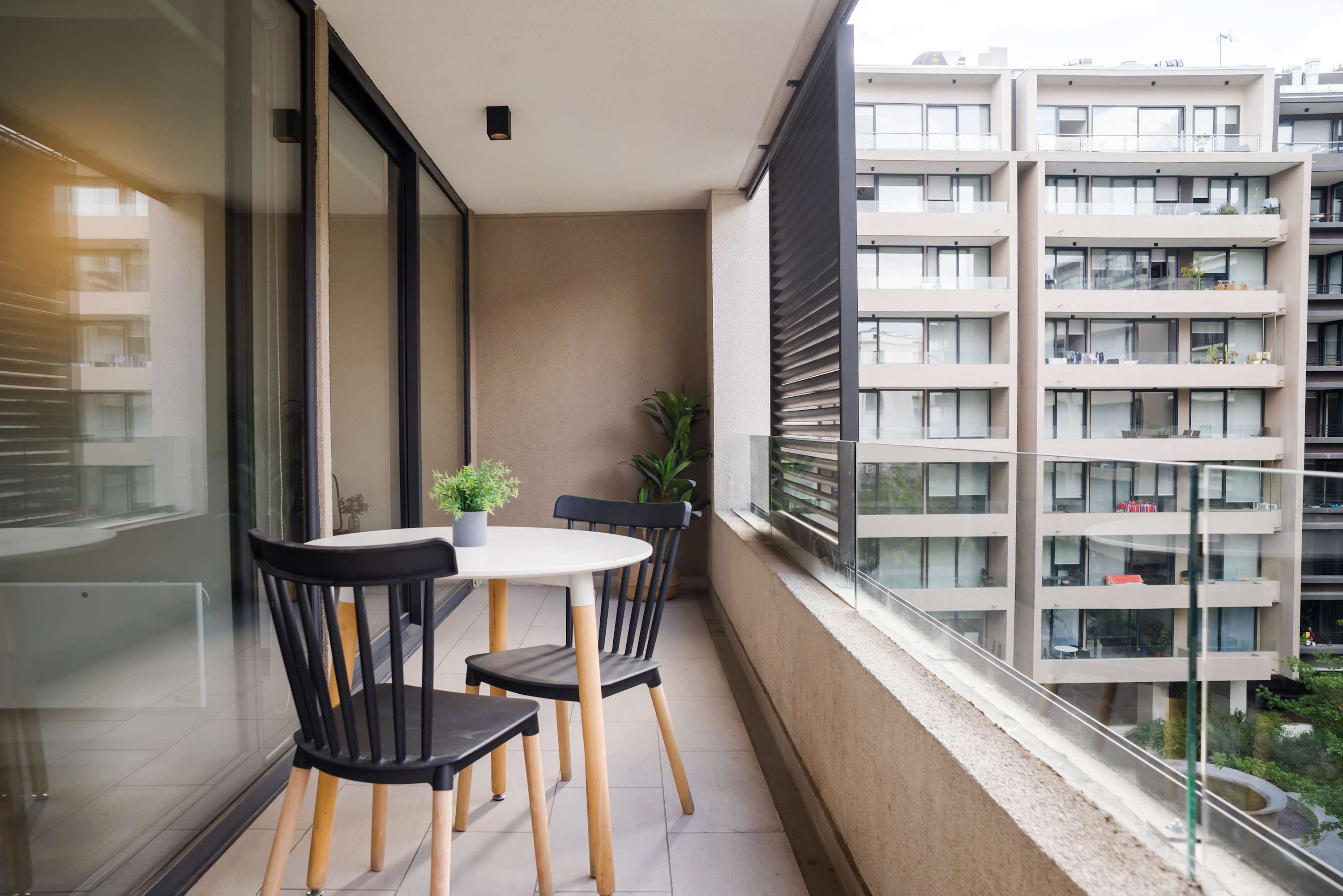 Private balcony with a round dining table, seating for outdoor meals, and leafy potted plants overlooking the modern courtyard.
