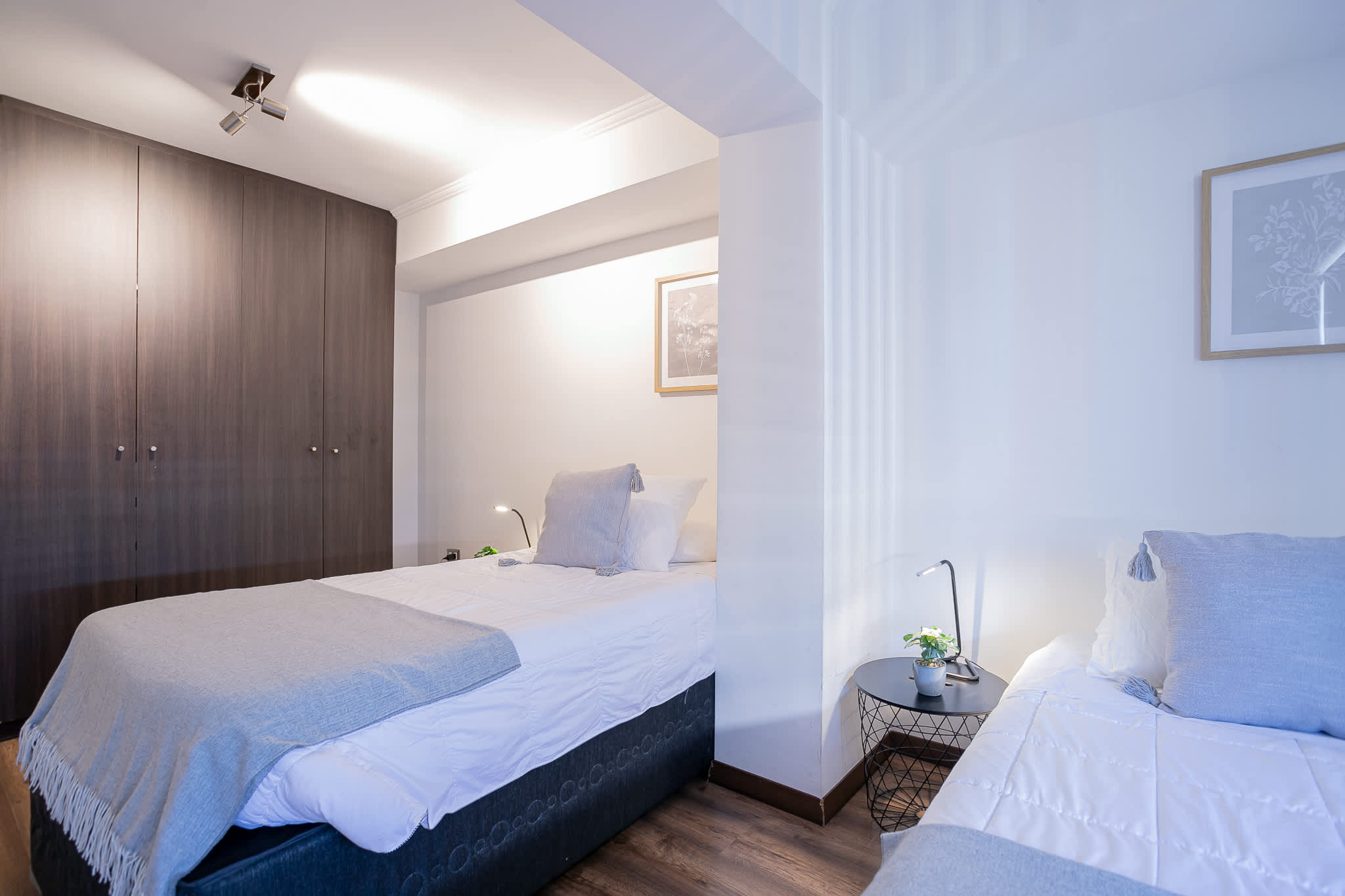 Private bedroom with crisp white bedding, a soft blue-gray throw, full-height wardrobes, and a convenient bedside reading lamp.