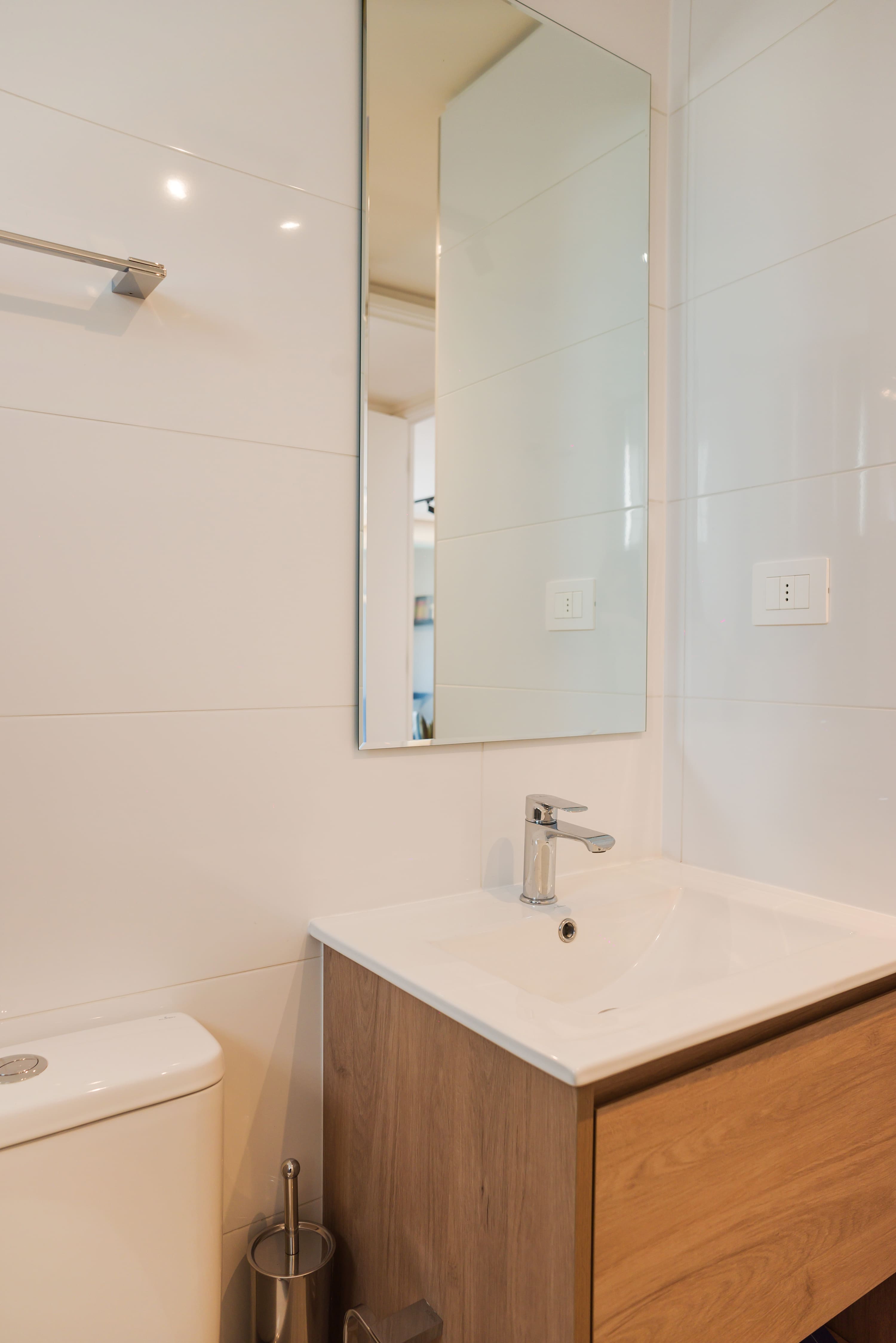 Modern bathroom with a mirrored cabinet, chrome faucet, white tile, and warm wood vanity details.