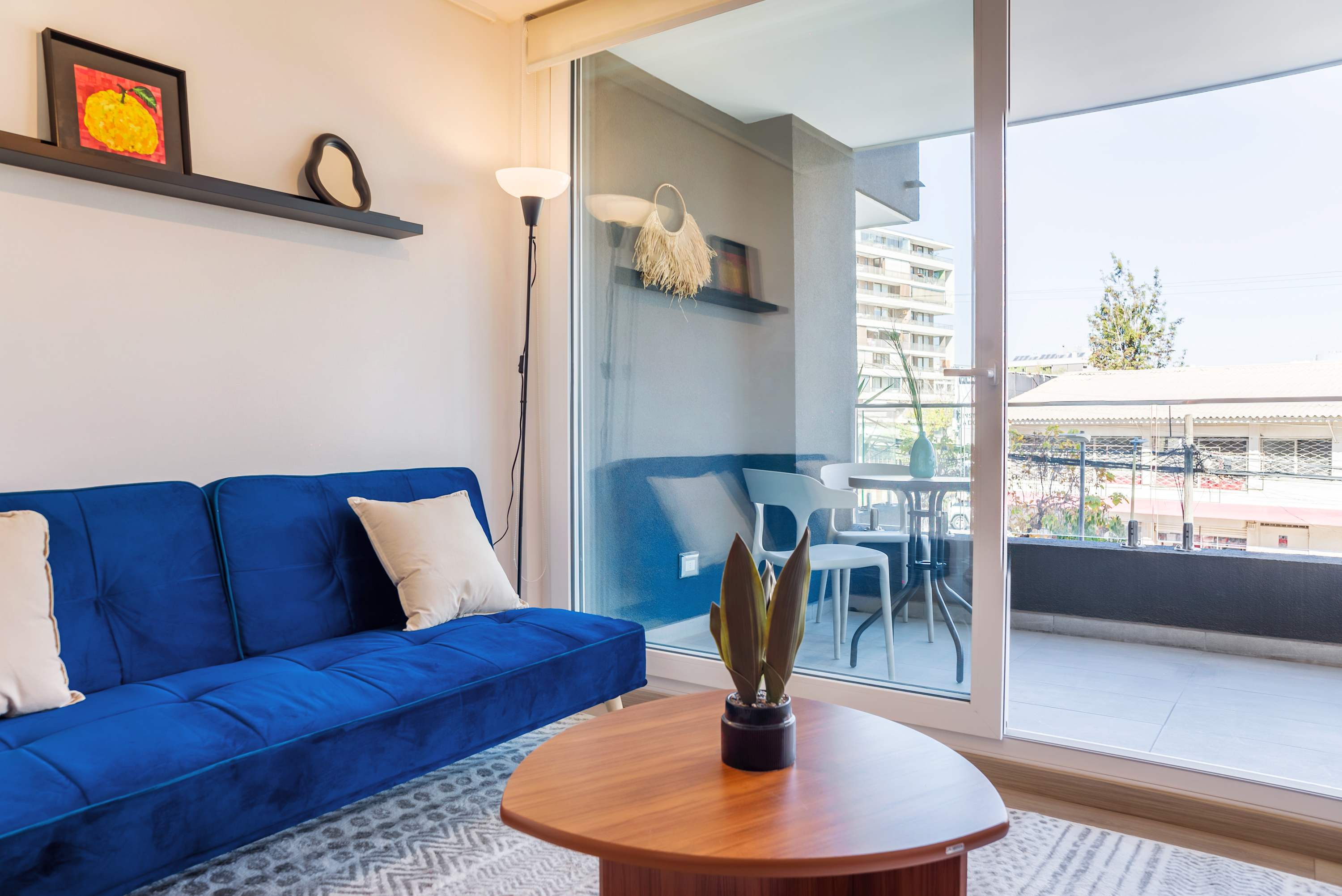 Bright living room with a royal-blue sectional and floor-to-ceiling glass doors opening onto a private balcony with outdoor dining.