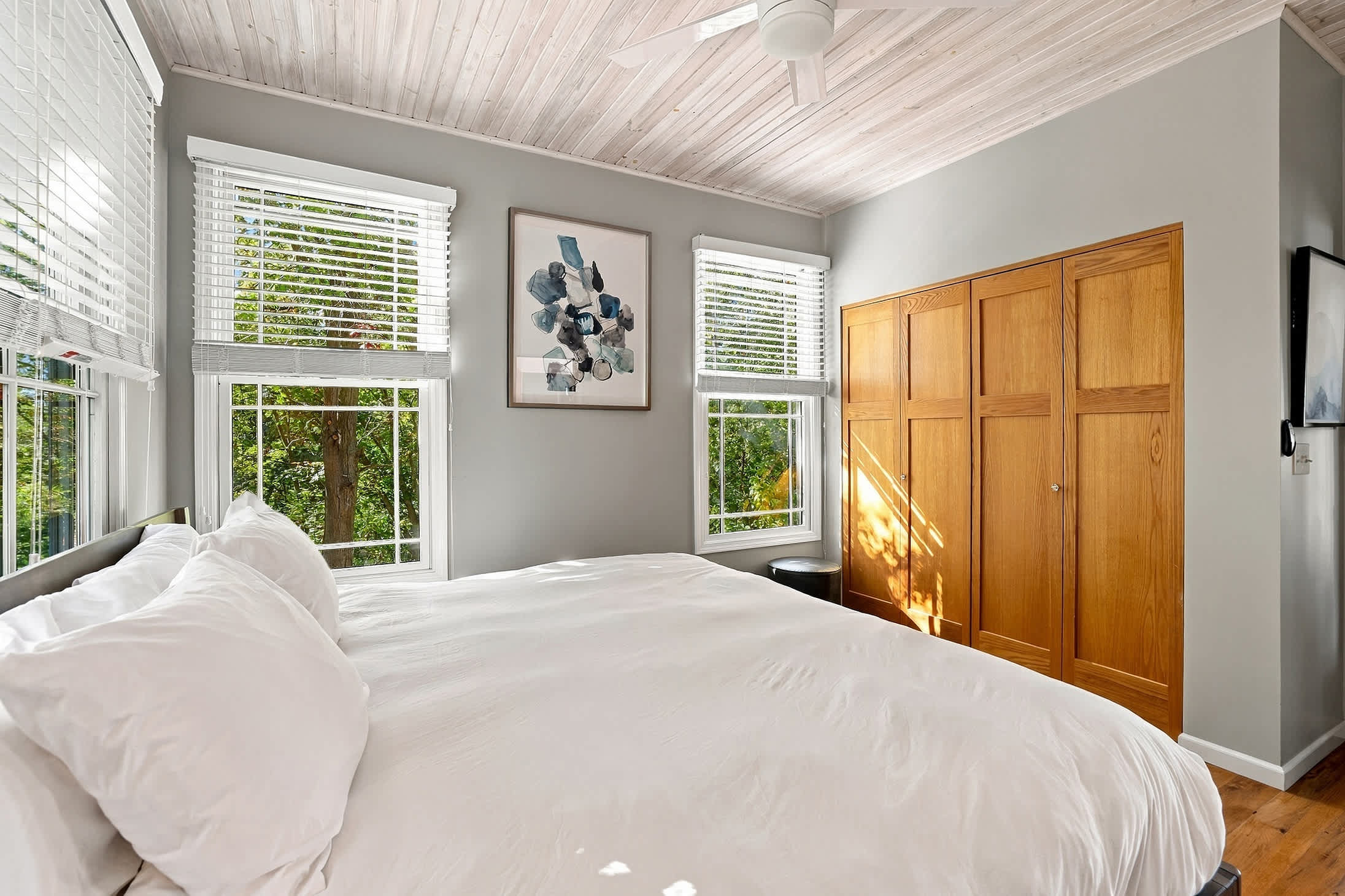 Sunlit bedroom framed by wooded views with ample closet space, a hidden TV inside, and tree views.