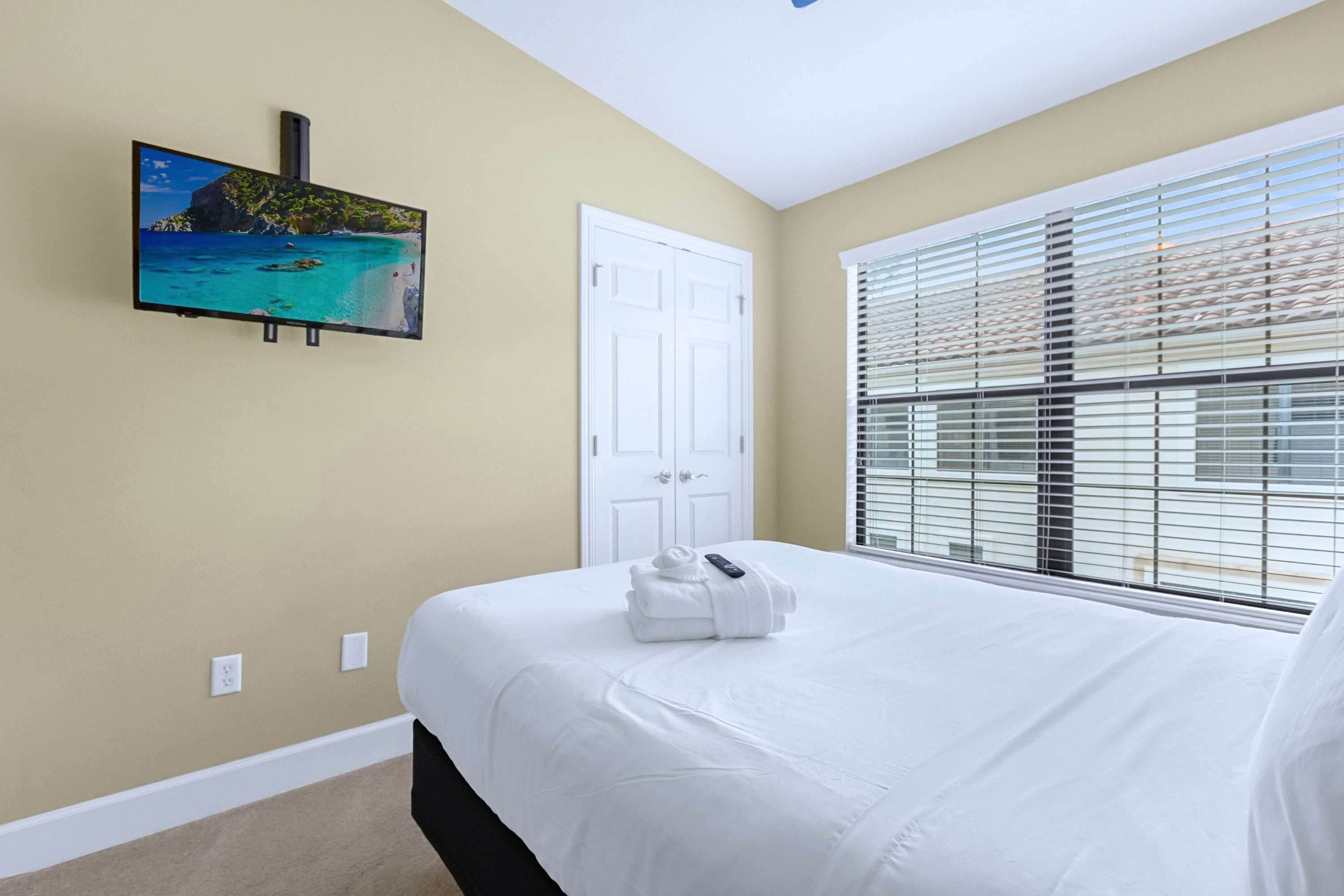 A peaceful guest bedroom featuring crisp white linens and a wall-mounted TV