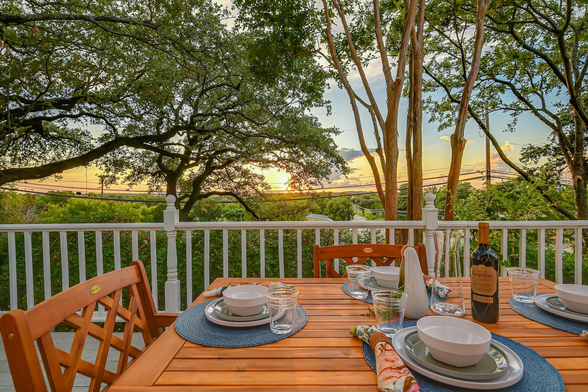 Enjoy serene outdoor dining on a private sunlit deck surrounded by lush trees and sunset views.