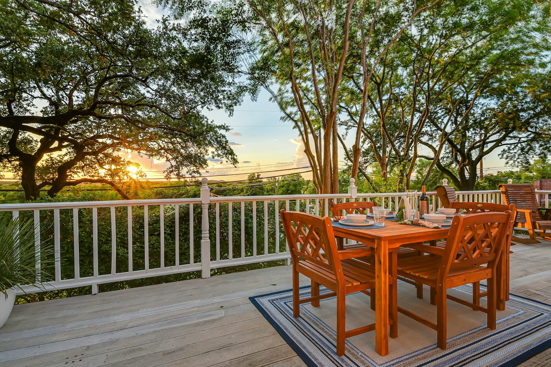 Enjoy serene outdoor dining on a private sunlit deck surrounded by lush trees and sunset views.