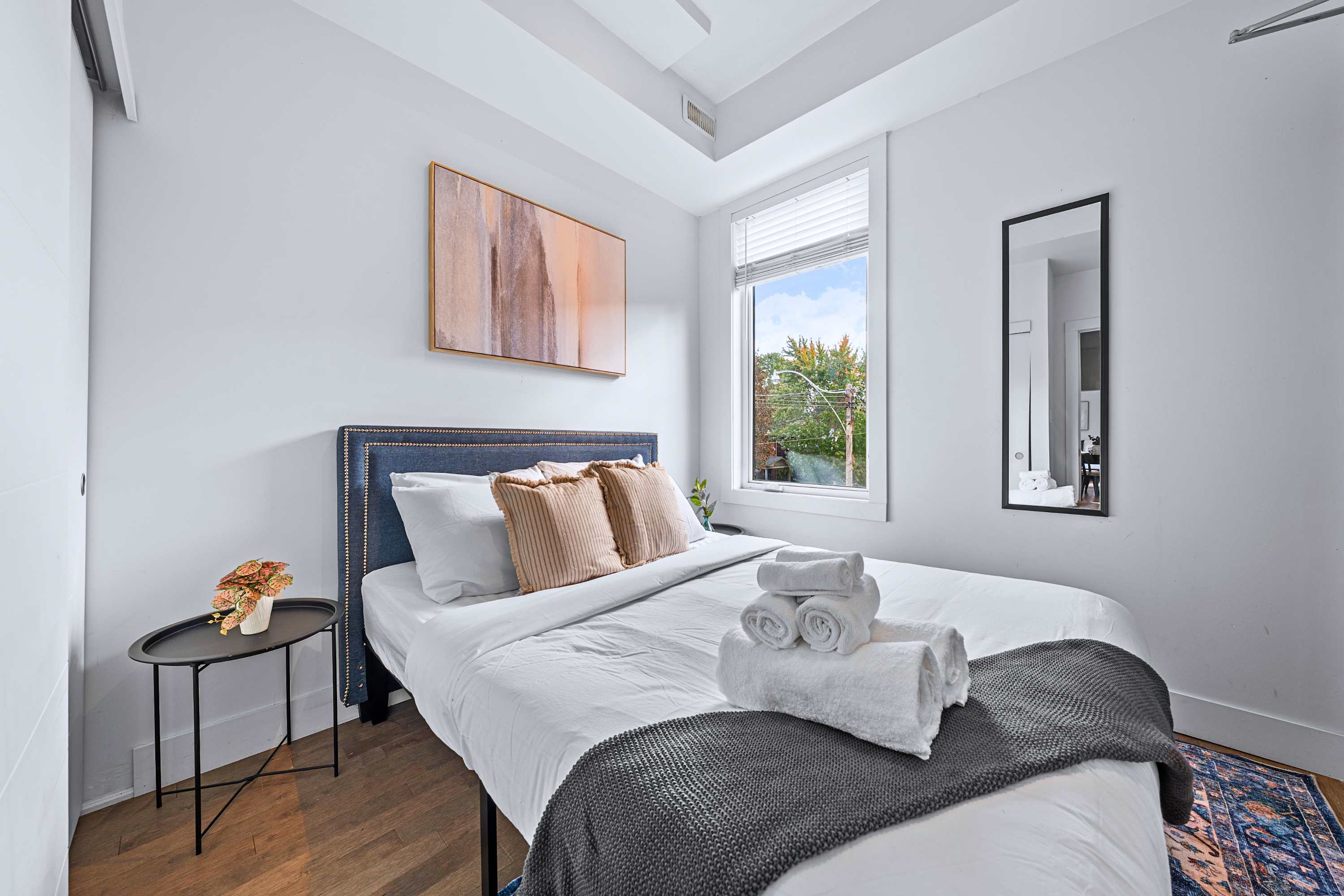 A sunlit guest bedroom offering a plush upholstered bed and crisp linens