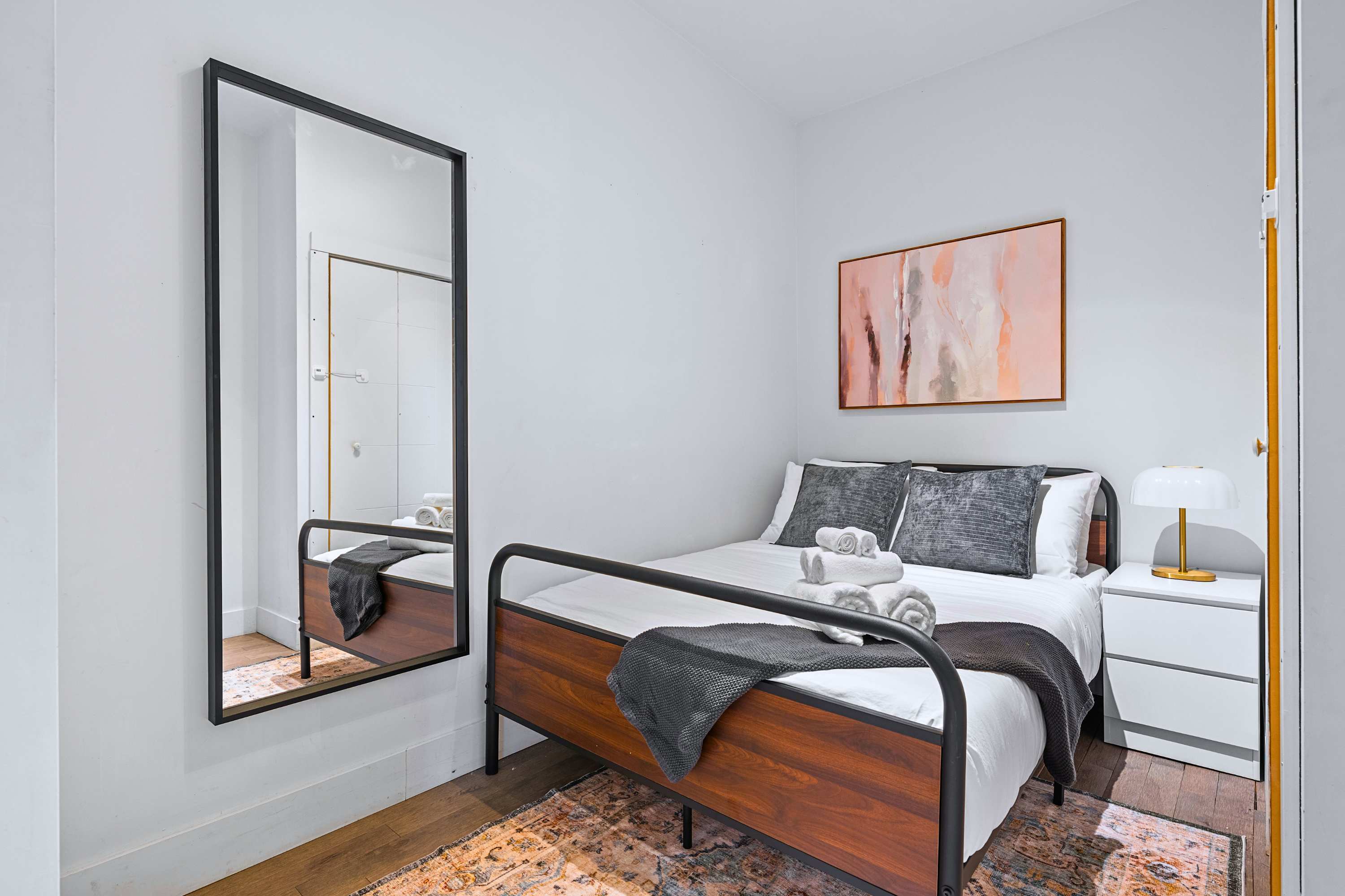 A bright guest bedroom equipped with a dark metal bed frame and large mirror