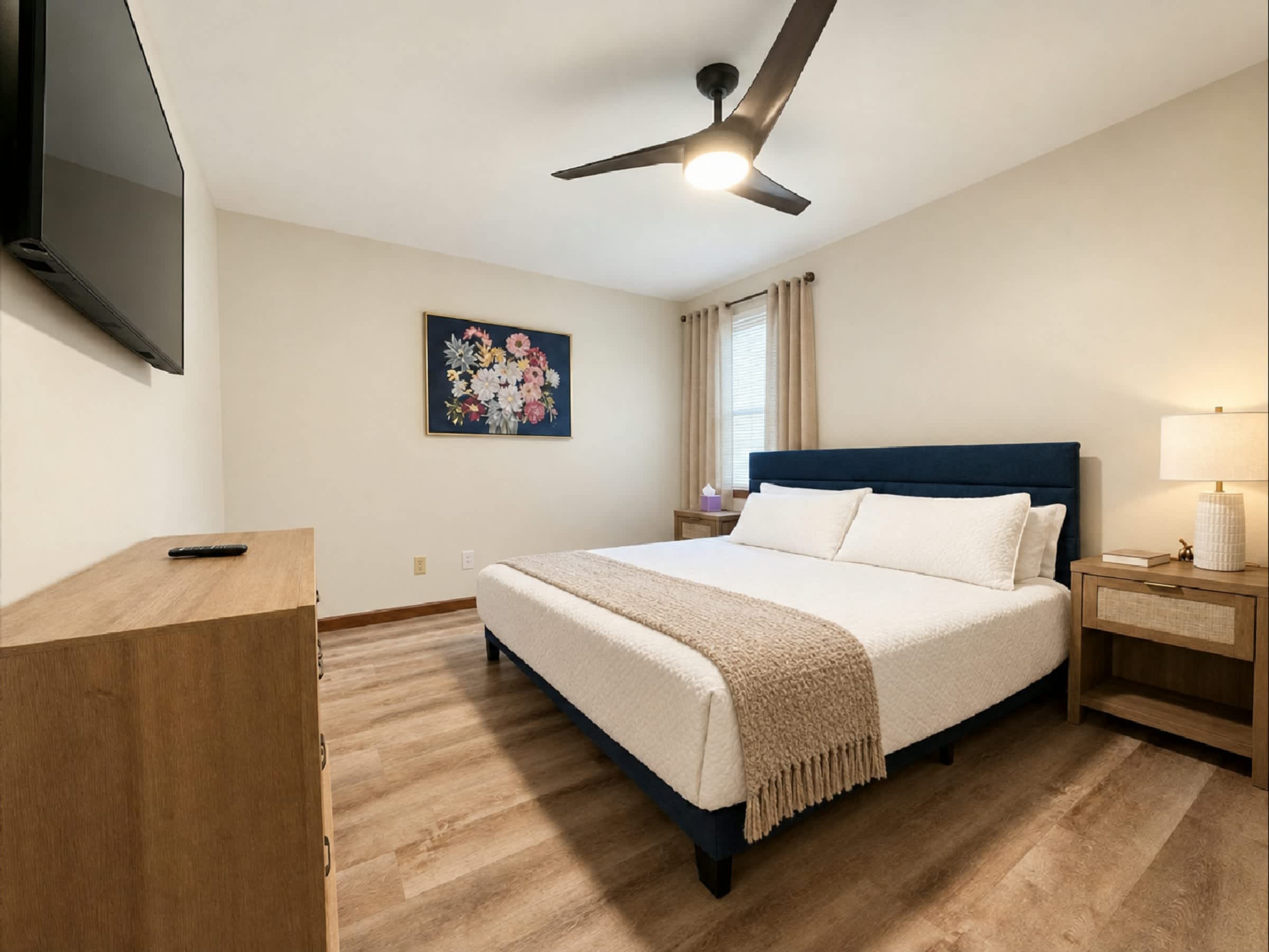 Relax in this spacious primary bedroom featuring a comfortable bed, smart TV, ceiling fan, and stylish furnishings. A peaceful retreat for a restful night's sleep after exploring Downtown Hamilton, Ohio.