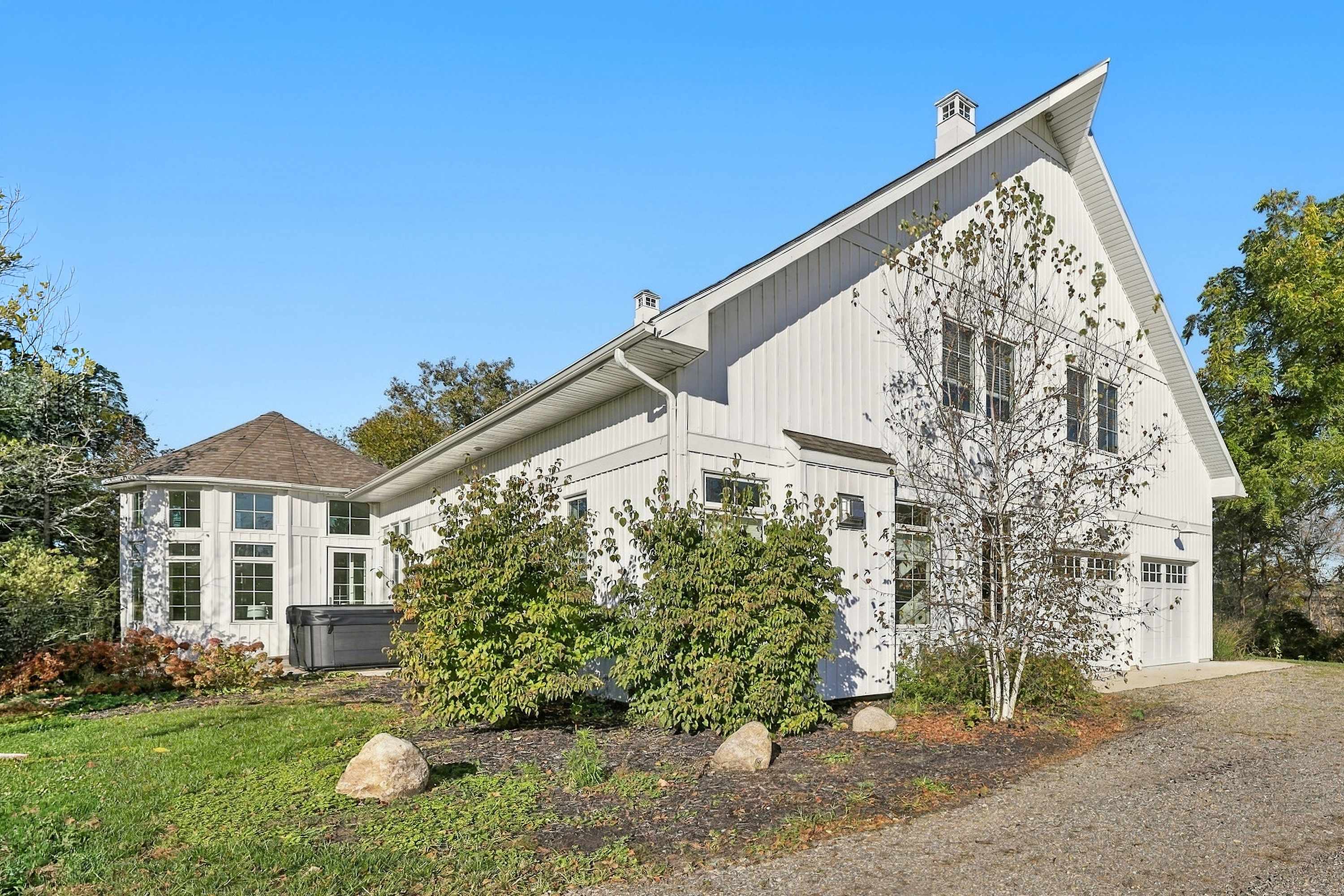 The Barn in Three Oaks, with a gravel drive, attached garage, and hot tub.
