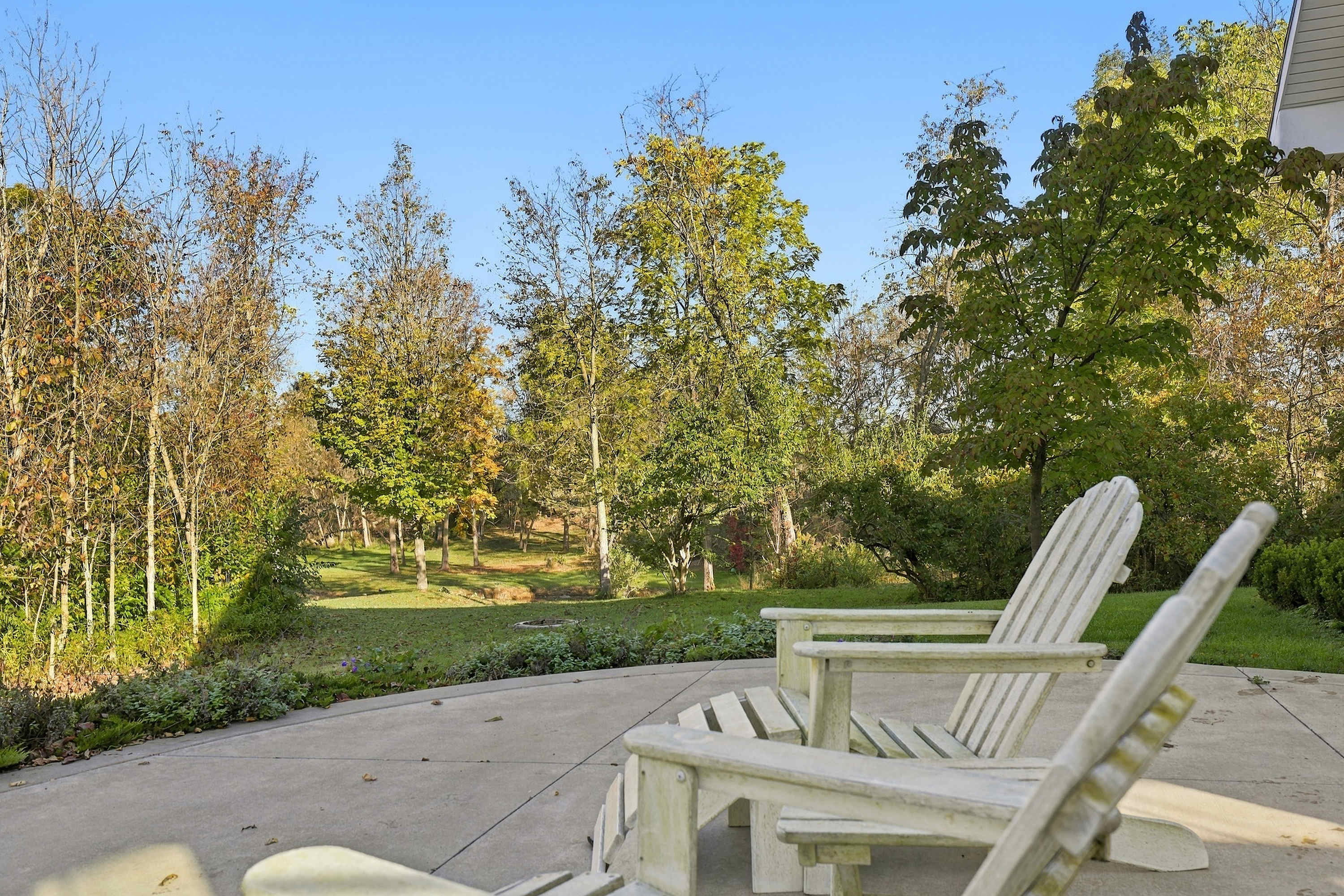 A Three Oaks patio overlooking the lawn, the fire pit, and the pond beyond.