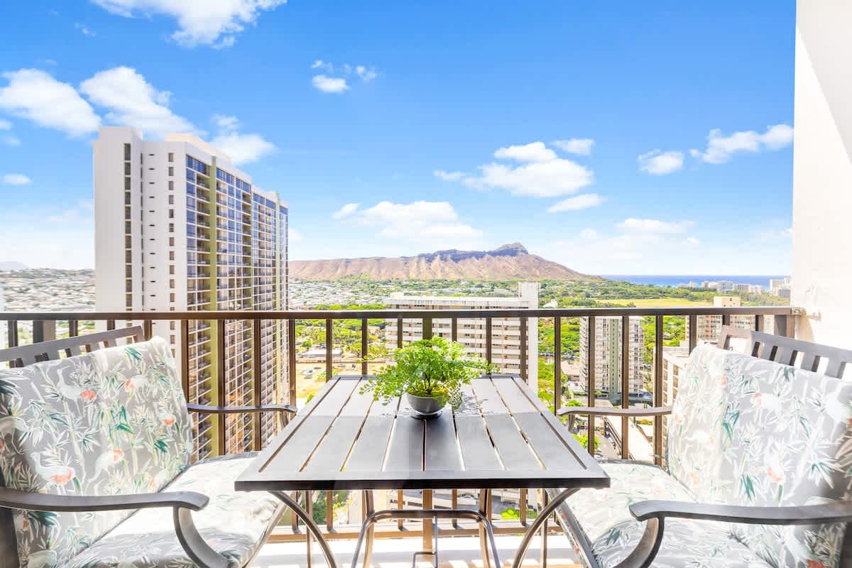 Balcony seating area with a view of the city skyline and distant mountain.