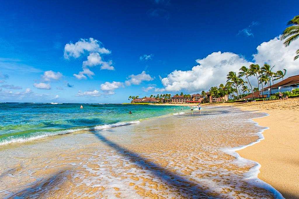 Turquoise waters gently wash onto the white sandy beach at Kiahuna Plantation, creating the perfect backdrop for a relaxing day by the ocean.
