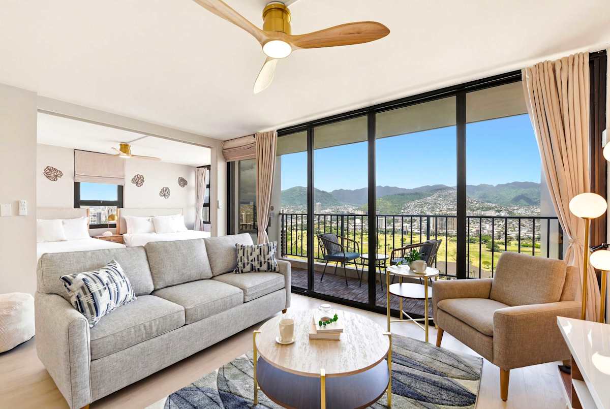 Your living area features chic, comfortable seating and expansive floor-to-ceiling glass doors that reveal a private balcony with sweeping mountain views.