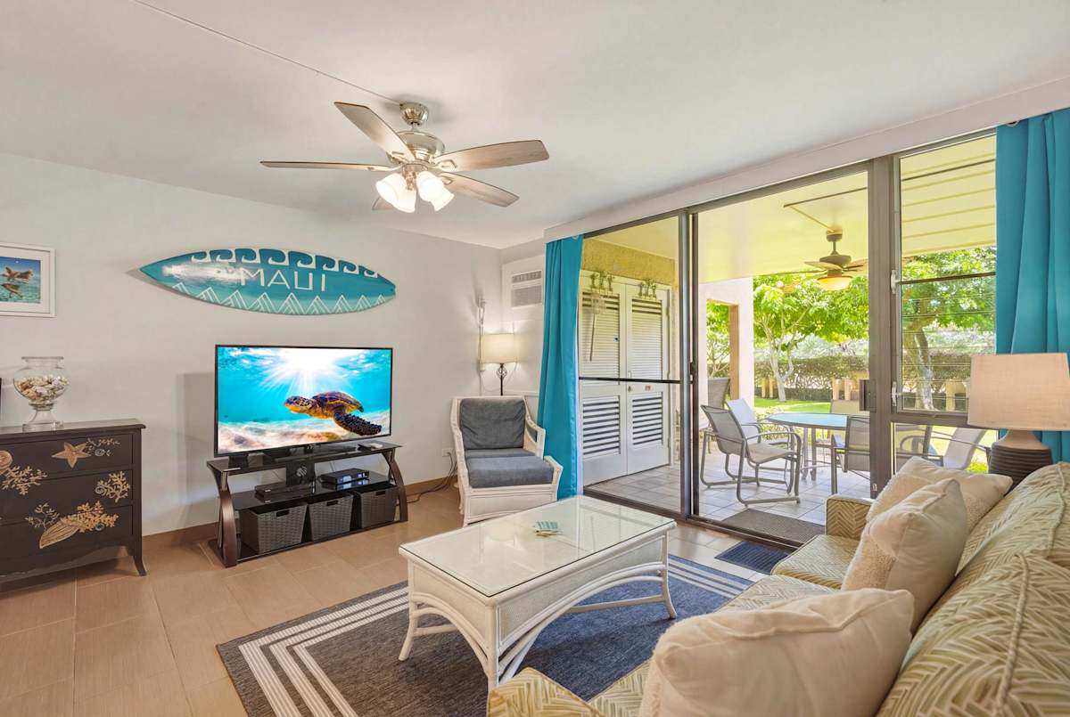 Relax in your bright, island-themed living room featuring a sleeper sofa, a flat-screen TV, and sliding glass doors that open directly to a covered outdoor patio.
