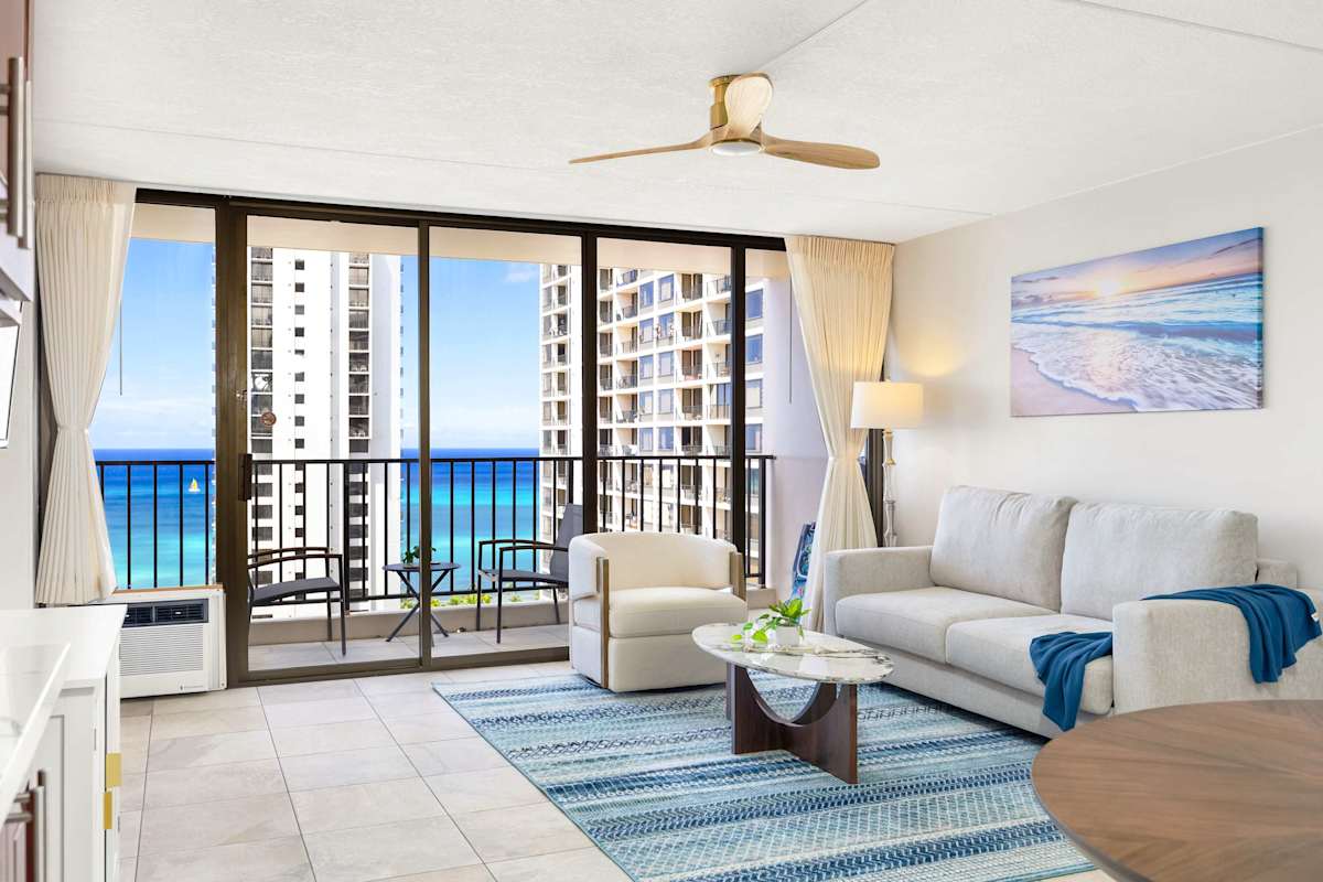 Your bright living room has a pull-out sleeper sofa, a coffee table, a ceiling fan, and large glass doors that open to a balcony with ocean views.