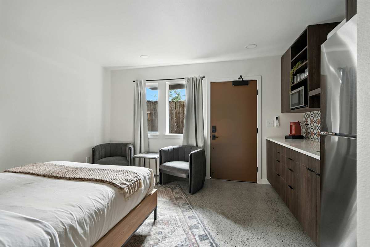 A compact hotel room with a bed, kitchenette, and sitting area.