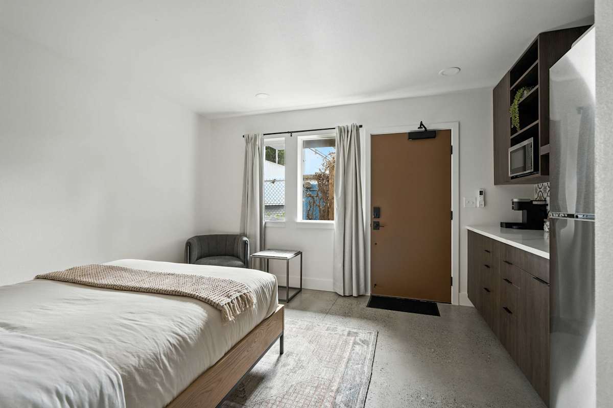 A hotel room with a bed, chair, table, window, door, refrigerator, and microwave.