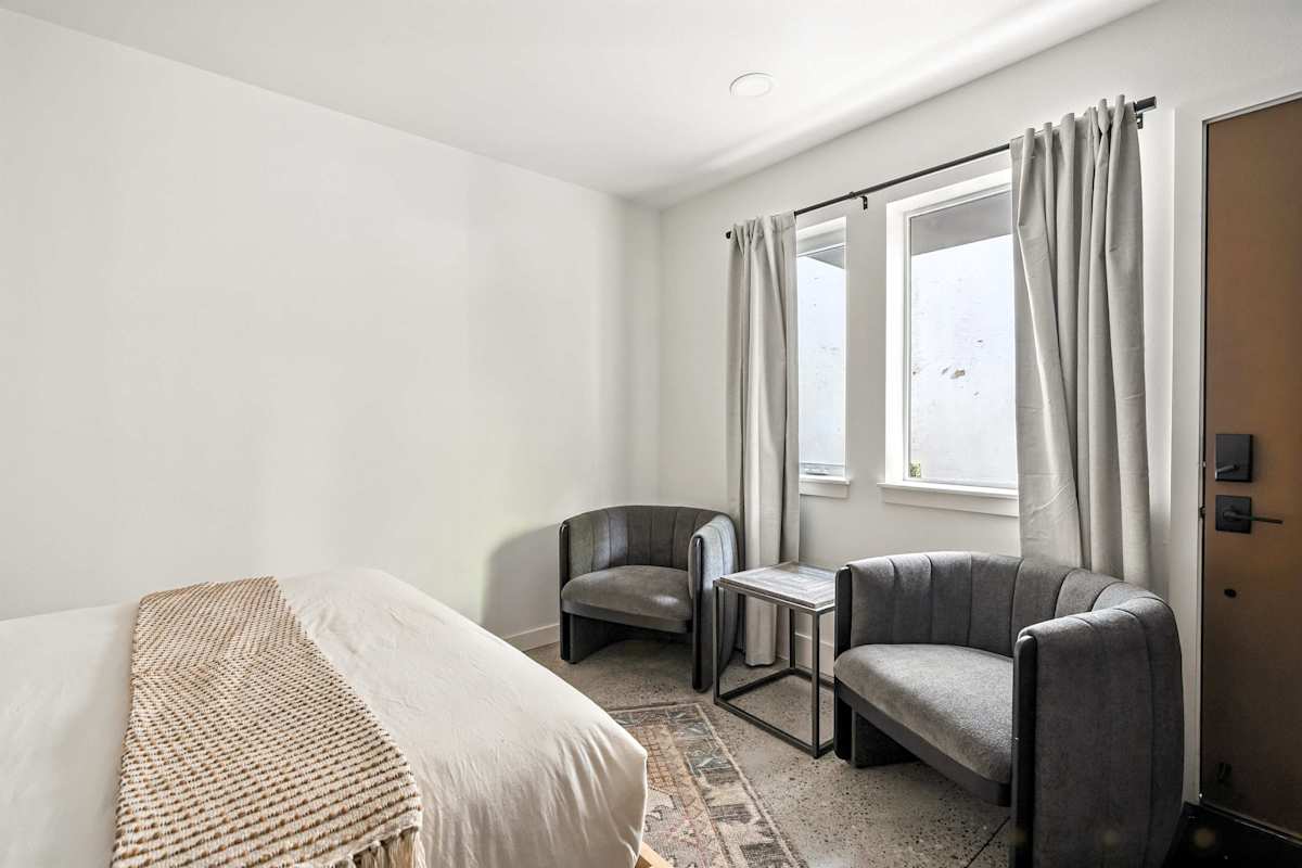 A hotel room with a bed, chair, sofa, and window.