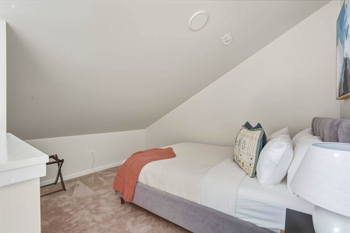 A neatly made bed in a small room with white walls and a slanted ceiling