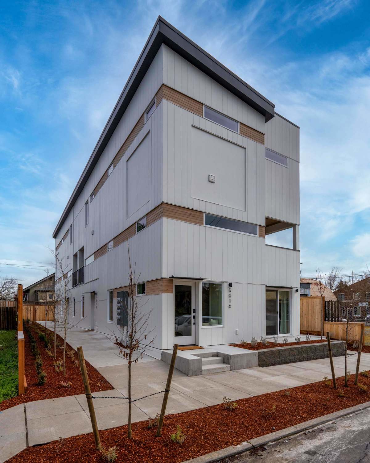 A modern, white, three-story building with a flat roof and a small front yard.